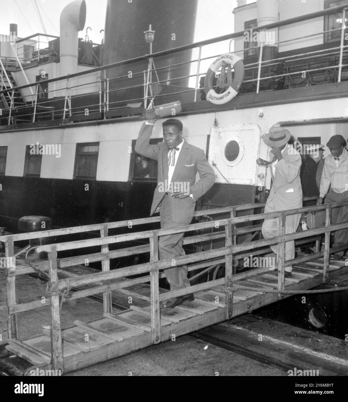 Southampton Hampton: Dieser jamaikanische Mann benutzt seinen Fall, um seinen Kopf vor dem Regen zu bedecken, während er die Gangway des Tenders "Balmoral" hinunterkommt, gefolgt von anderen Passagieren heute. Die „Balmoral“ hatte die Immigranten aus ihrem Schiff geholt, das wegen schlechtem Wetter in Cowes Roads vertäut war. Der Immigrant hatte bei gutem Wetter die Westindischen Inseln im 'Montserrat' verlassen, aber bei der Ankunft hier regnete es sehr stark und viele hatten nur leichte Sommerkleidung. 24. Oktober 1961 Stockfoto