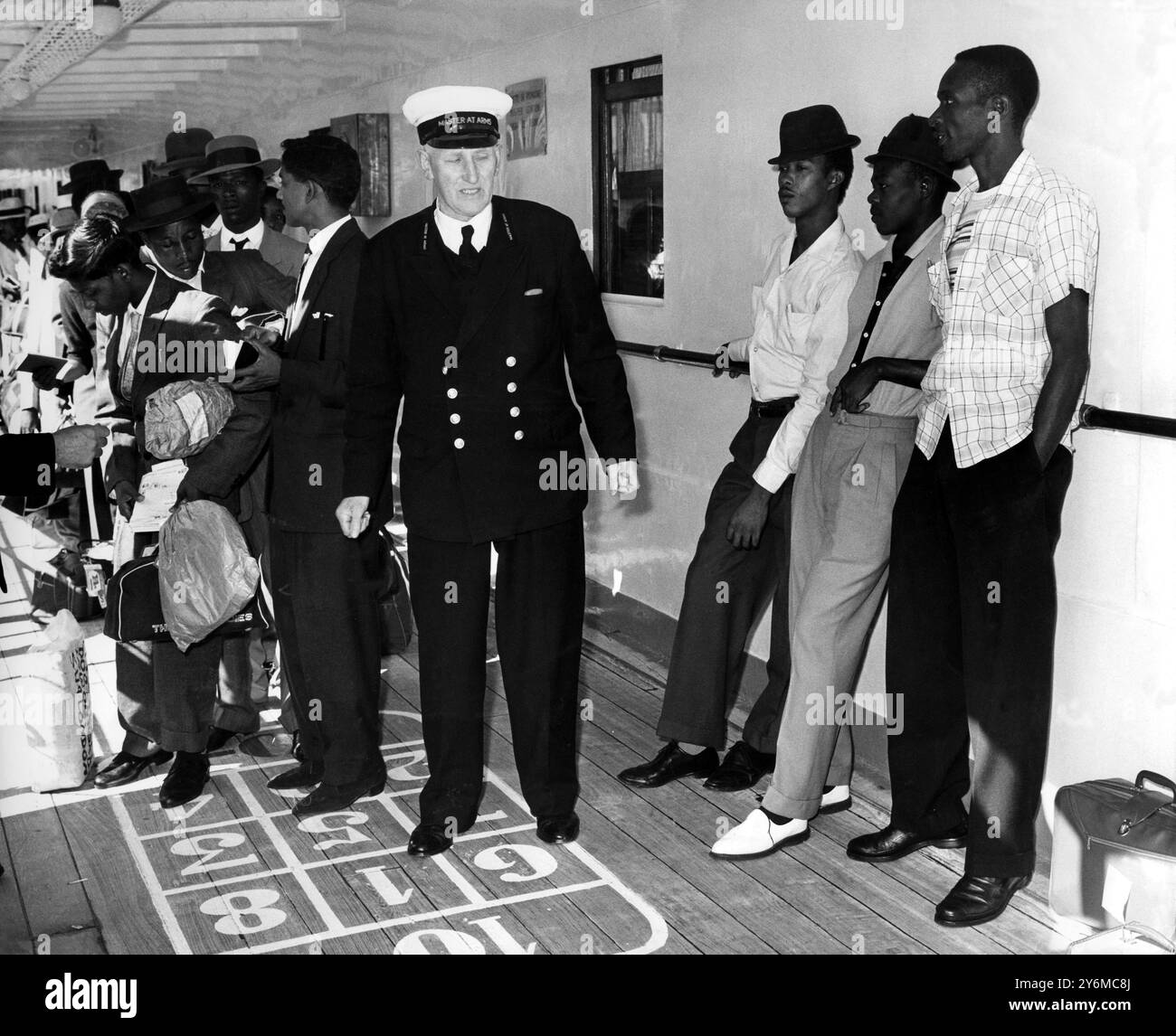 Das neue Leben beginnt mit einem Überfall für Westindianer-blinde Passagiere. Juni 1962. Während andere Westindianer vom italienischen Linienschiff Ascania in Southampton an Land gehen, lehnen sich die drei jungen Männer auf der rechten Seite unter dem Auge eines Waffenmeisters gegen ein Schott. Sie waren blinde Personen, die es geschafft hatten, während der Reise entdeckt zu werden, wurden aber vom Waffenkapitän des Schiffes festgenommen, als sie versuchten, ohne Landkarten an Land zu gehen. Die Ascania hatte etwa 1.100 Einwanderer an Bord – die größte Zahl, die Großbritannien in einer einzigen Partei aus Trinidad, Barbados und St. Kitts erreichte. Sie kamen nur eine Woche vor dem an Stockfoto