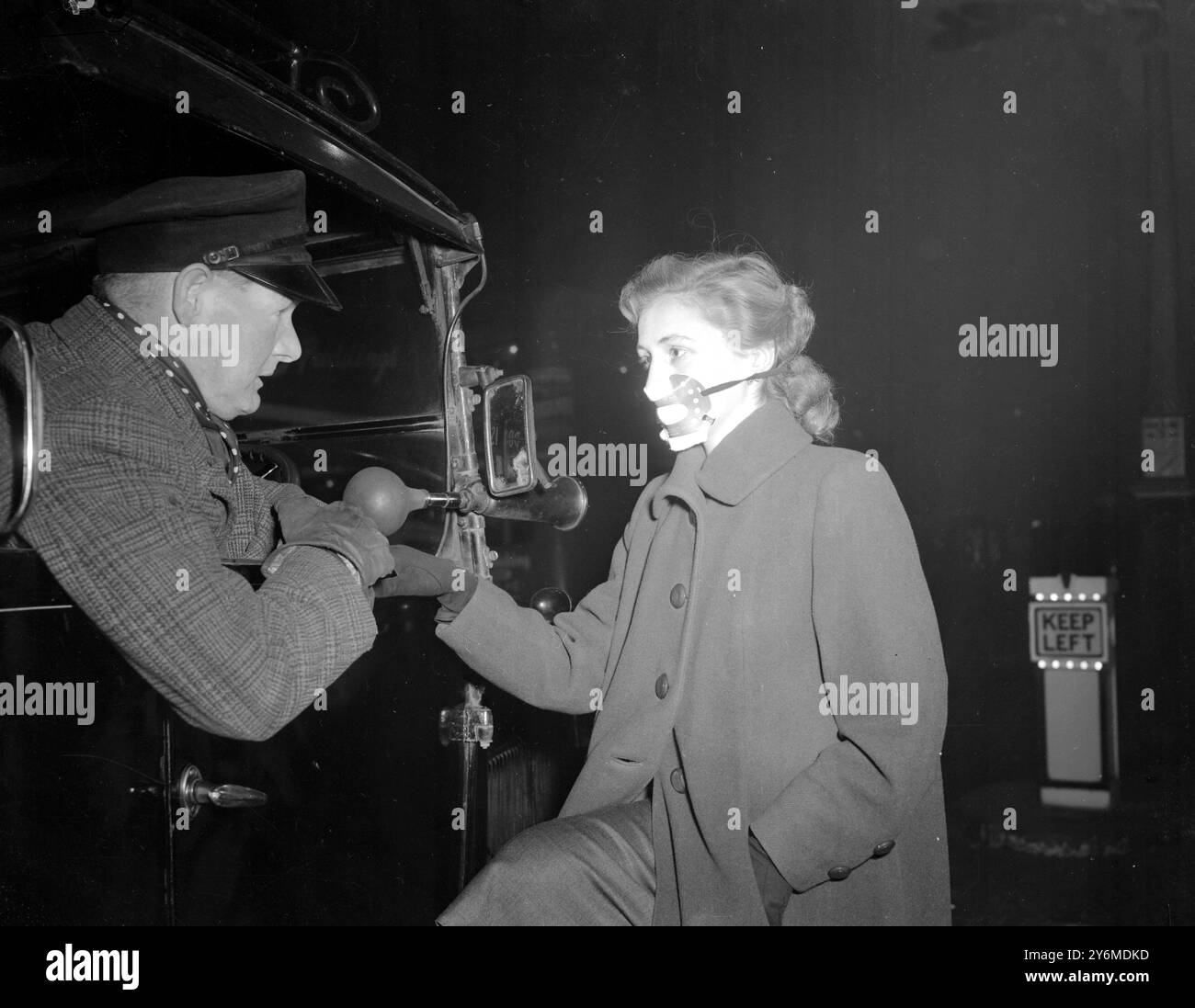 London: Kein Überfall in The Strand, sondern Pamela Dalton aus Peckam, der mit Cabby Charles Cody plaudert. Pamela trägt eine Schutzmaske gegen die Wahrscheinlichkeit von Smog, während Nebel die Hauptstadt bedeckt. 17. November 1953 Stockfoto