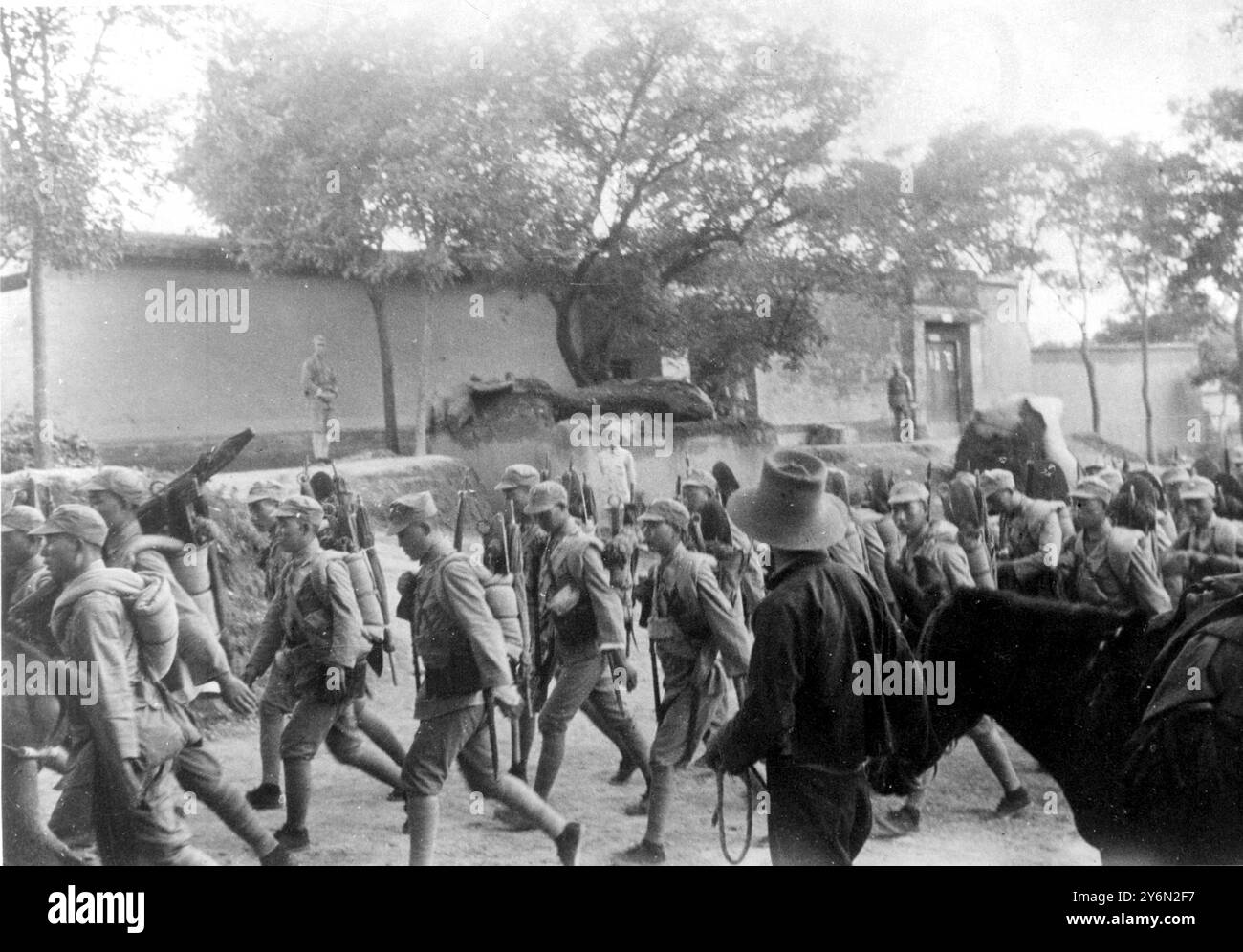 Chinesische Truppen - Gewehre und Decken schwebten über ihre Schultern und marschierten durch ein Dorf nördlich von Shanghai, auf dem Weg zur Verteidigung von Nanking, der Hauptstadt, die jetzt von den Japanern bedroht ist. Diese Truppen mussten sich aus Shanghai zurückziehen und eilten nach Norden, um Nankings Verteidigung zu verstärken. 21. November 1937 Stockfoto