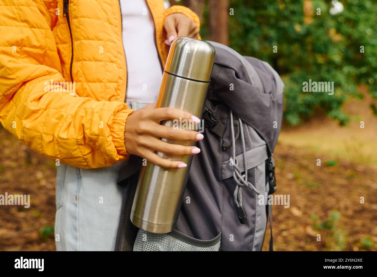 Eine junge Afroamerikanerin hält eine Thermoskanne bei der Erkundung der lebhaften Herbstwälder, umgeben von der Natur. Stockfoto