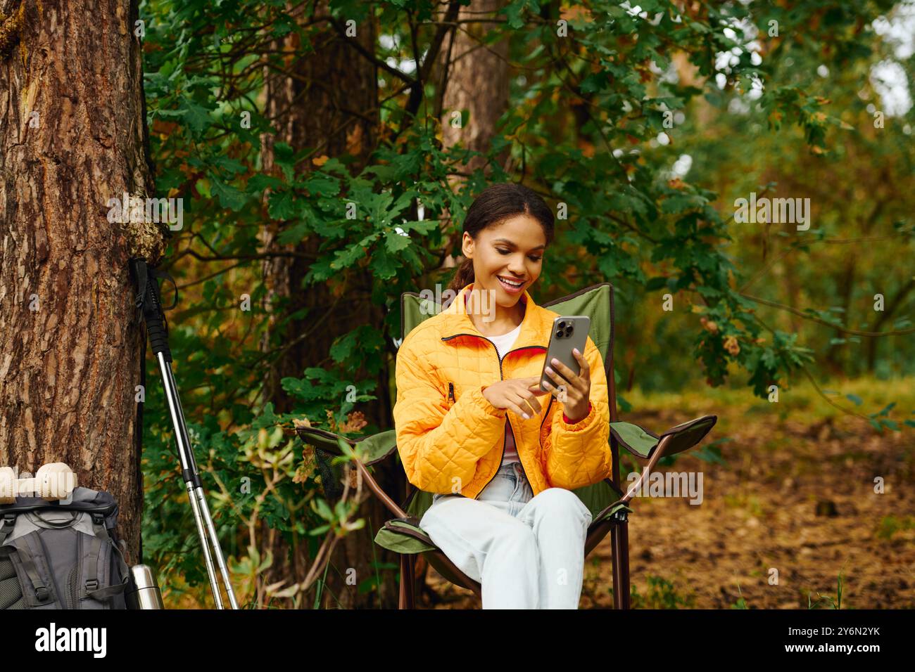 Umgeben von leuchtenden Herbstfarben entspannt sich eine junge Frau, während sie im Wald ihr Handy überprüft. Stockfoto
