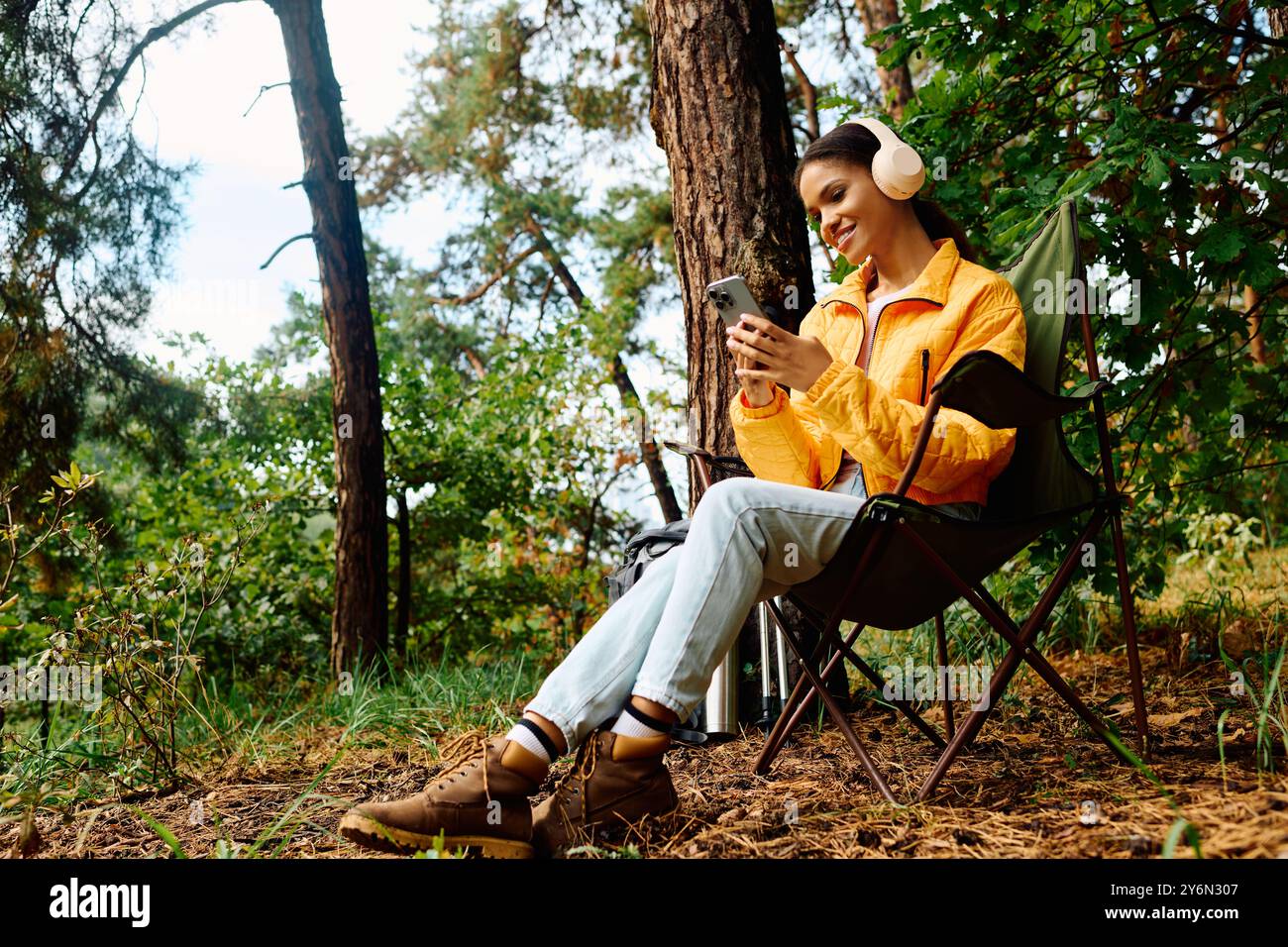 Eine junge Frau entspannt sich in einem Stuhl, ganz in Musik eingetaucht, während sie durch farbenfrohe Herbstwälder wandert. Stockfoto