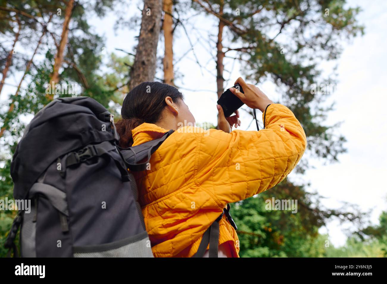 Auf dem Weg durch einen bunten Wald hält eine junge Frau das strahlende Herbstlaub mit ihrer Kamera fest. Stockfoto