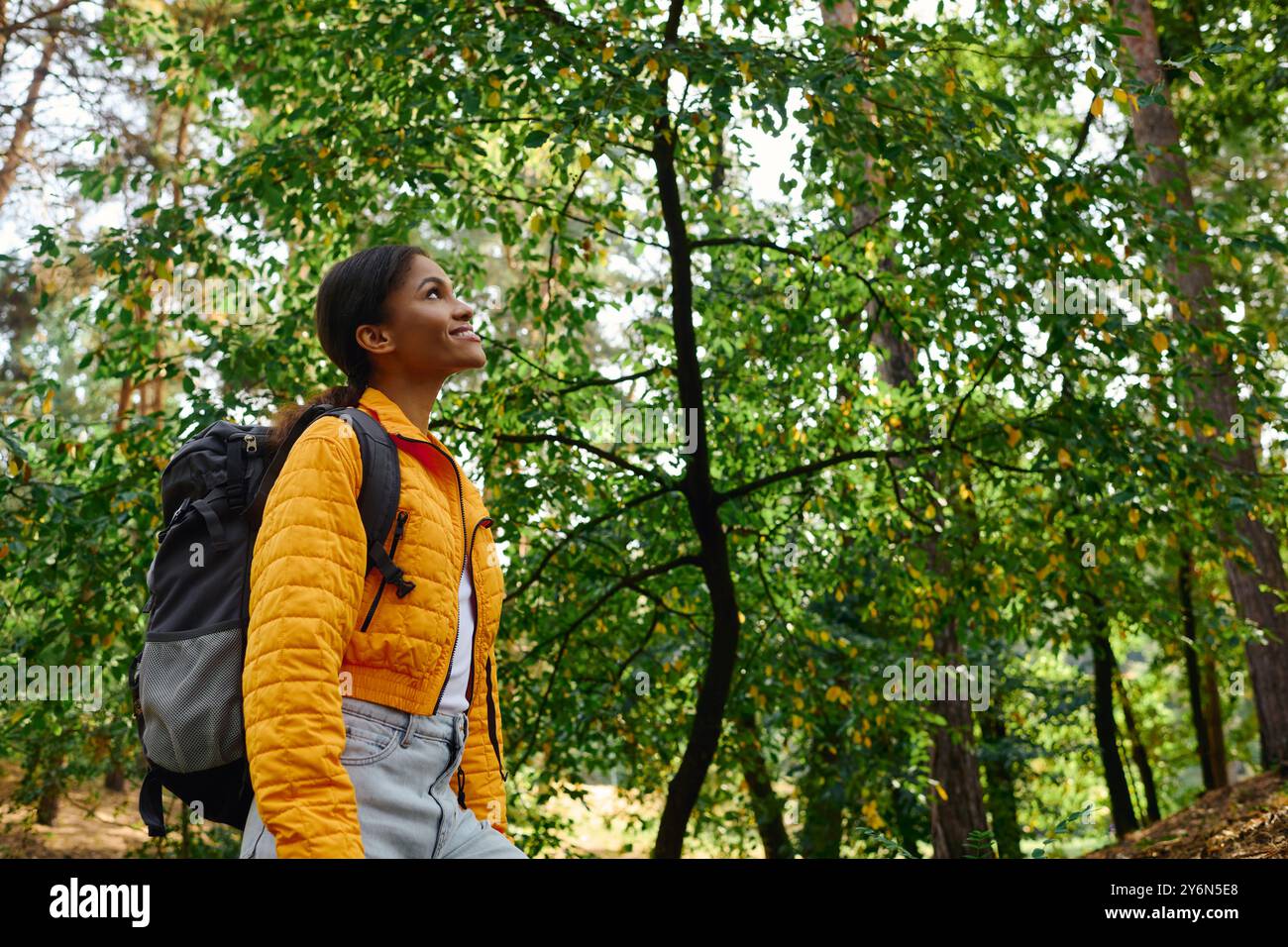 Eine junge Afroamerikanerin erkundet an einem Herbsttag einen üppigen Wald und strahlt Freude und Abenteuer aus. Stockfoto