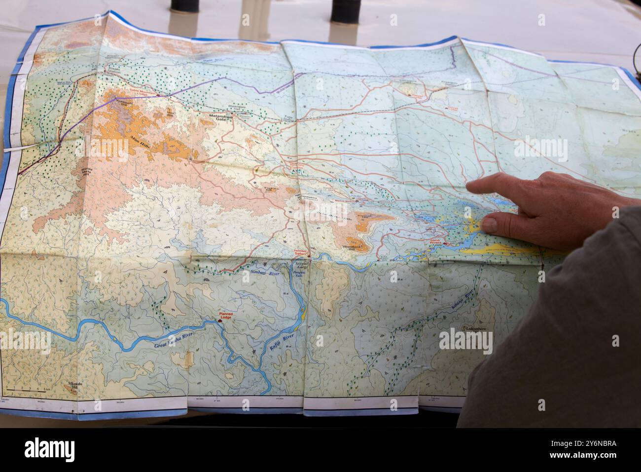 Eine Person zeigt auf eine detaillierte topografische Karte, die die Navigation und Erkundung erleichtert. Die Karte zeigt Gelände, Flüsse und Reiserouten, was einen andeutet Stockfoto