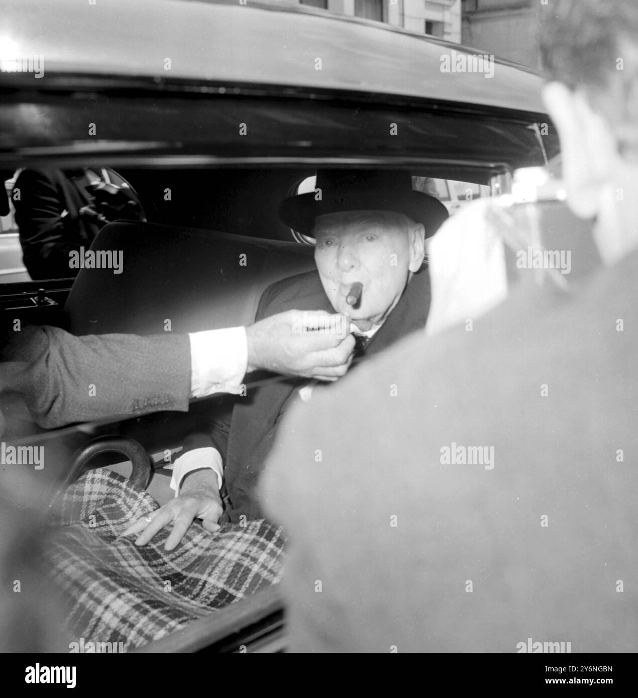 London: Ein Assistent hält ein Spiel für Sir Winston Churchills Zigarre aus, als Britians ältester Staatsmann heute sein Hyde Park Gate hier verlässt, um an der erwarteten letzten Fragestunde im House of Commons teilzunehmen. Sir Winston Churchill wird morgen nicht im Haus sein, wenn Sir Alec Douglas-Home, der Premierminister, eine Allparteienanordnung vorlegt, in der Sir Winston Churchill für seine Dienste für Parlament und Nation gepriesen wird. Nachdem der Antrag genehmigt wurde, wird Sir Alec eine kleine Deputation zu Sir Churchills Haus führen, um die Bedingungen des Antrags zu übermitteln. Sir Alec wird Sir Winstons geschriebenes R vorlesen Stockfoto