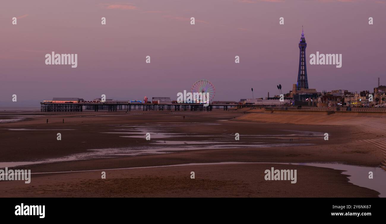 Die Abenddämmerung fällt über einen ruhigen Strand, mit einem Pier und einem Riesenrad, das sich am Abendhimmel abhebt. Stockfoto