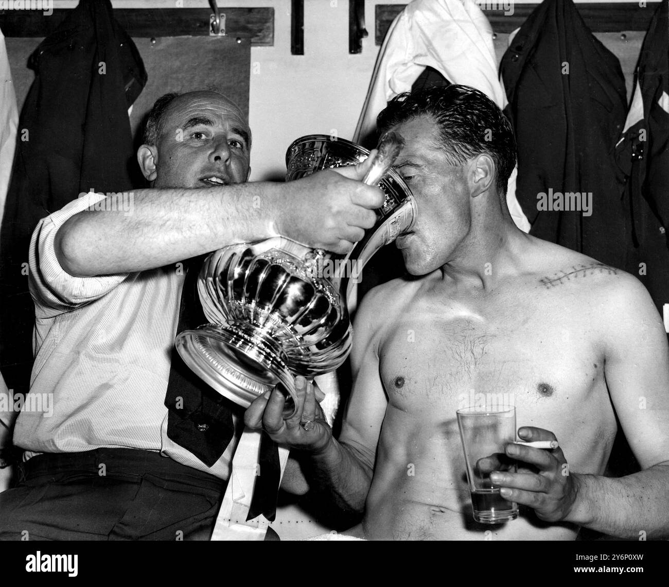 3. Mai 1958: Die Finalsieger des FA Cups. Bolton Wanderers (2) gegen Manchester United (0). Foto-Shows: Der Kapitän und Mittelstürmer der Bolton Wanderers, Nat Lofthouse, der beide Tore seines Teams erzielte, erhält einen Drink von seinem Manager Bill Ridding in der Garderobe von Wembley. Eine Reihe von Stichen ist auf Lofthouse's Schulter zu sehen, wo eine Nadel nach seiner kürzlichen Verletzung eingeführt wurde. Stockfoto