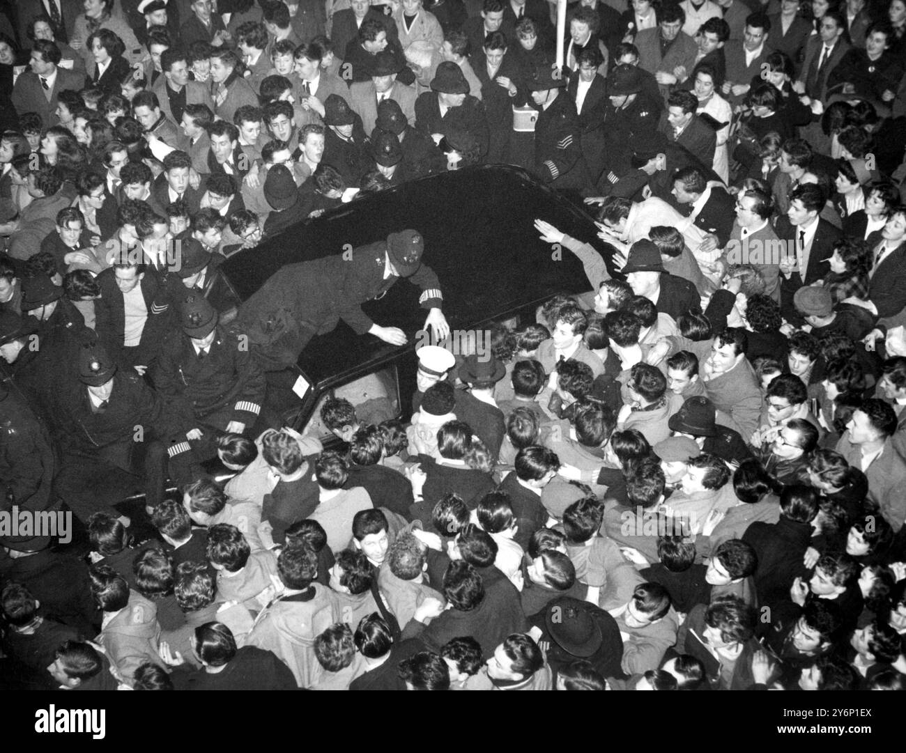 Ein Polizist, der auf dem Dach des Autos liegt, und andere auf der Motorhaube versuchen, in Schacht A zu halten drängen tausende von rasenden Fans und erzwingen eine Passage für den amerikanischen Rock'n'Roll-König Bill Haley Ankunft in Waterloo Station London heute Abend der Bandleader - hier für eine Tour durch Großbritannien mit seiner Band The Comets - war von Southampton in einem Spezialzug mit 400 Fans hochgefahren, nachdem sie von der Cunard ausgestiegen waren die Königin Elizabeth, die ihn am 5. Februar 1957 aus New York gebracht hatte Stockfoto