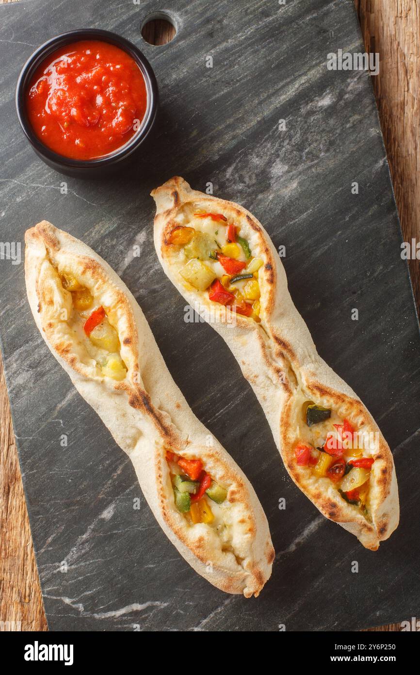 Pizza sorrentina Tomatenmozzarella und Gemüse wie Zucchini, Tomaten, Pfeffer, Artischocken auf dem Schieferteller auf dem Holztisch. Vertikal Stockfoto