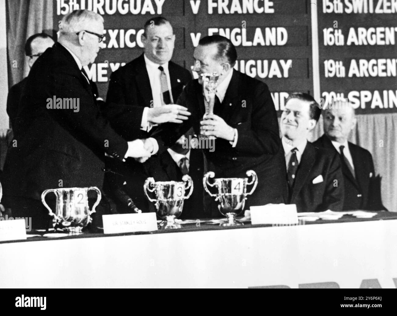 London: Sir Stanley Rous (links) Präsident der Fdederation of International Footall Association erhält den Jules Rimet Cup von Dr. Luiz Murgel. Vor der Auslosung für den diesjährigen würde Cup (rechts) steht Earl Harewood. 6. Januar 1966 Stockfoto