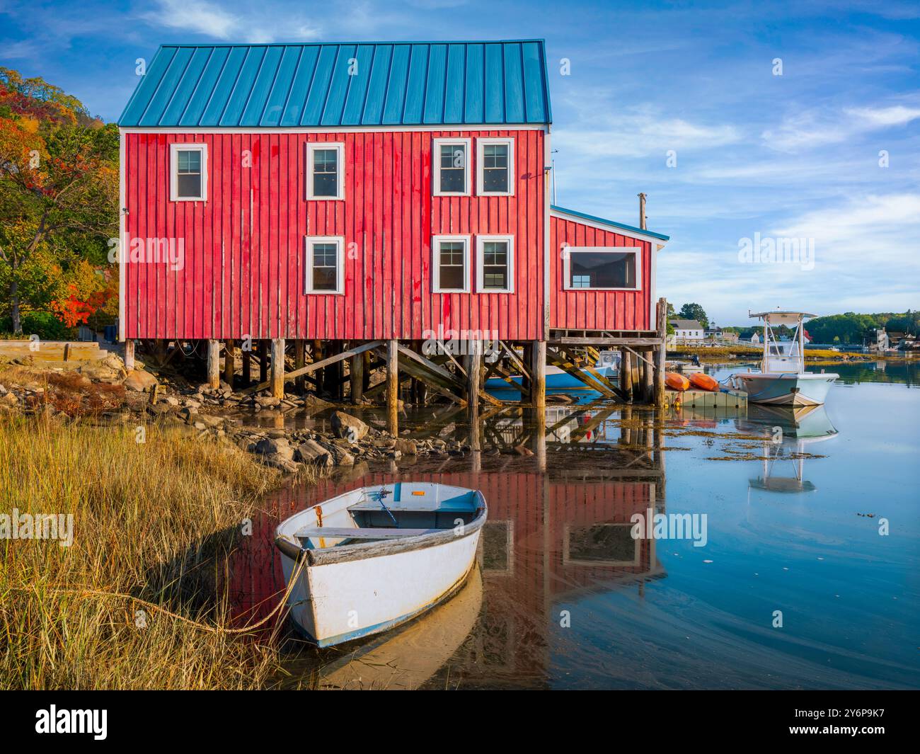 Rotes Holzgebäude auf Stelzen am Rand einer ruhigen Uferpromenade mit kleinen Booten in der Nähe. Die Szene enthält Reflexionen im Wasser und V Stockfoto