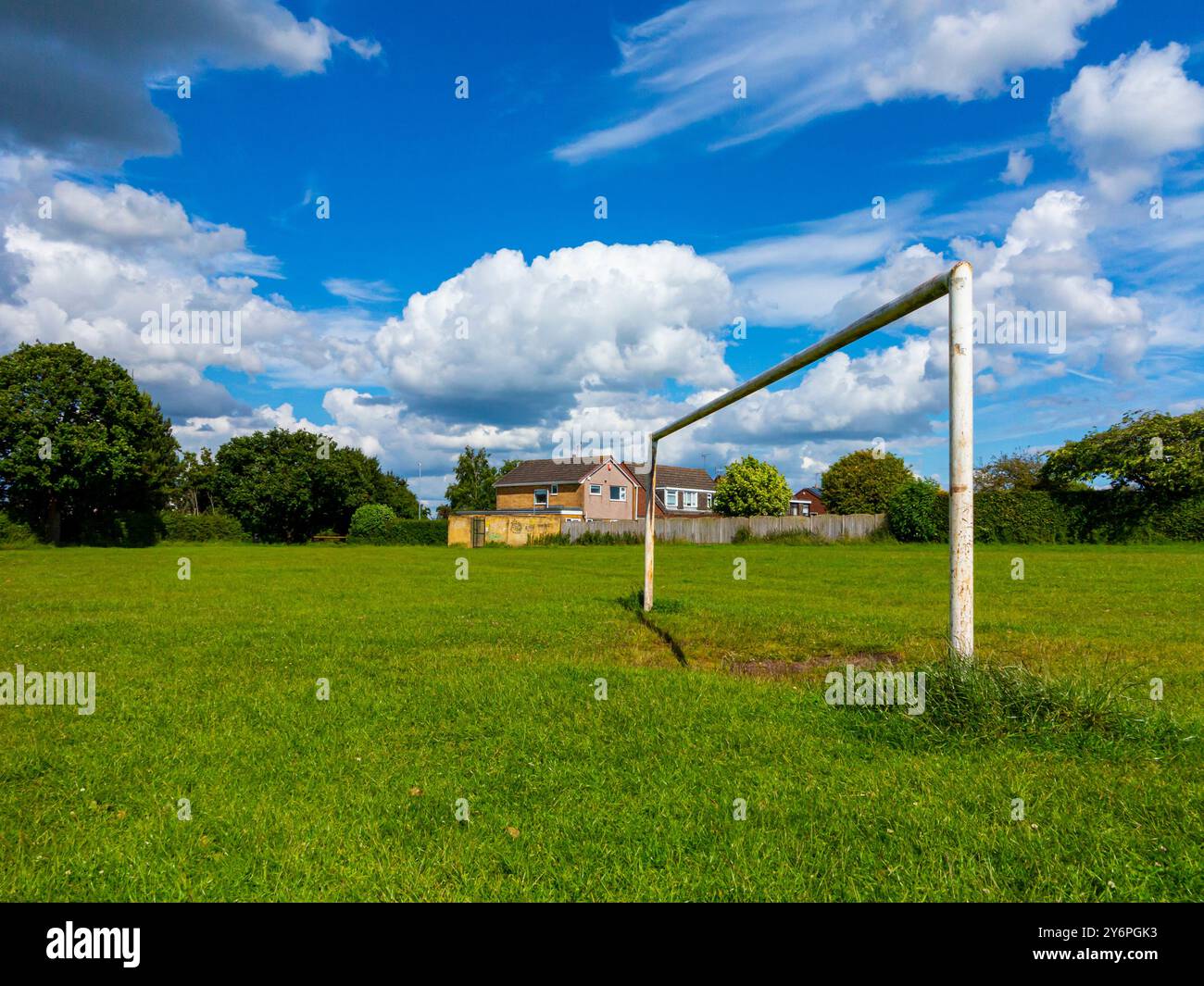 Torpfosten auf einem Fußball- oder Fußballfeld in einem Vorstadtpark mit Häusern dahinter und blauem Himmel mit weißen Wolken darüber. Stockfoto