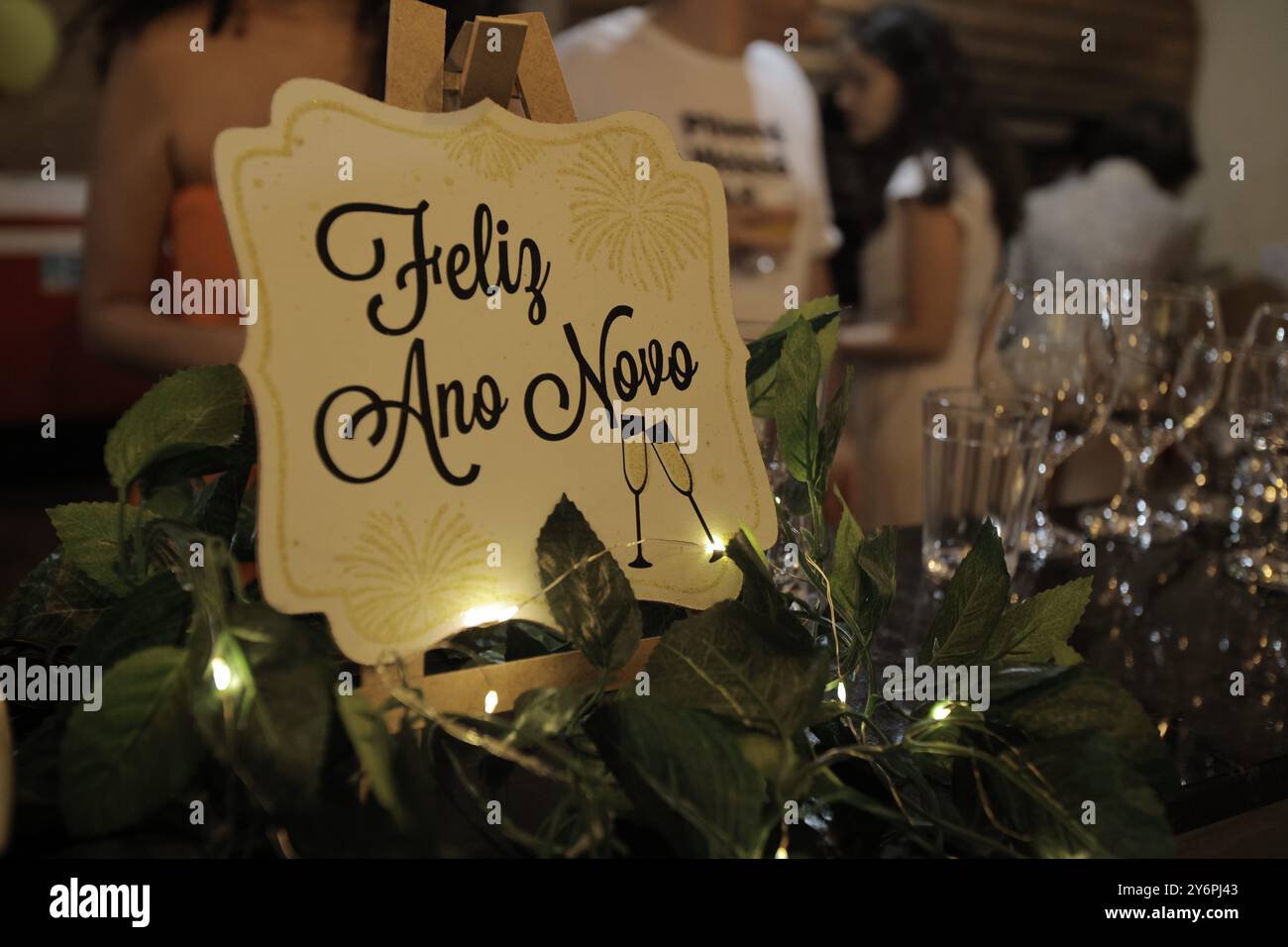 Ein Zeichen für ein glückliches neues Jahr mit den Worten „Feliz ano novo“. Das Schild ist von grünen Blättern umgeben und steht auf einem Tisch Stockfoto