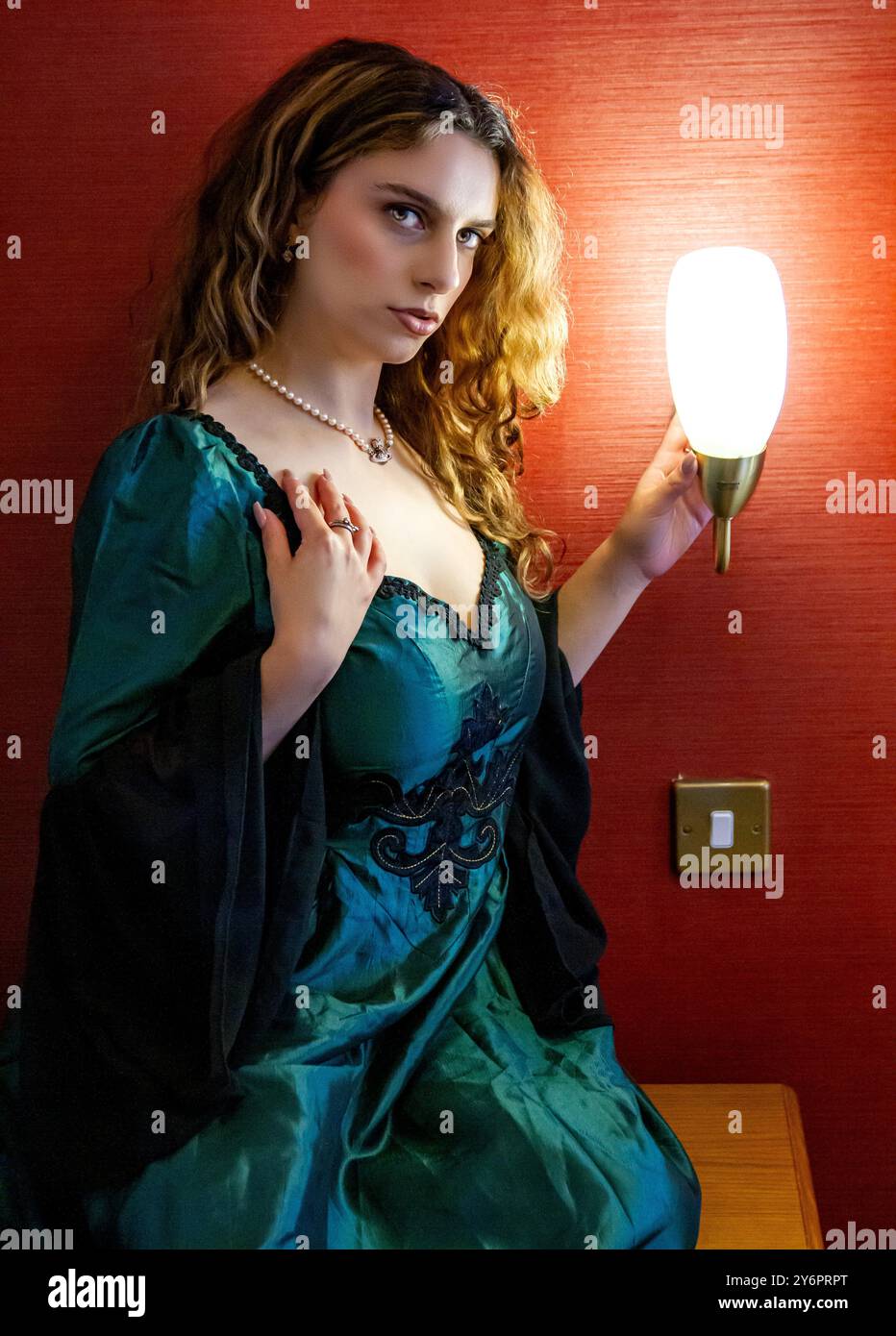 Ein hübsches weibliches Model sitzt neben einer hellen Nachttischlampe in einem Schlafzimmer im Dundee Queens Hotel und posiert für Fotos in Schottland Stockfoto Ein hübsches weibliches Model sitzt neben einer hellen Nachttischlampe in einem Schlafzimmer im Dundee Queens Hotel und posiert für Fotos in Schottland Stockfoto