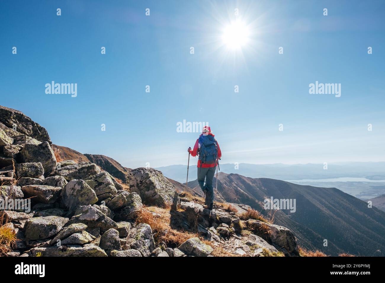 Backpacker-Frau in knallroter Jacke, die durch Bergketten mit Trekkingstöcken mit Hintergrund des Liptov-Tals geht, Westtatra, Slowakei. Aktive p Stockfoto