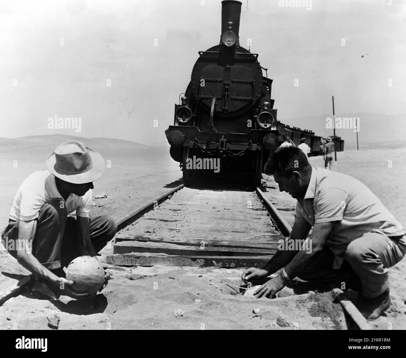 SABOTEURE BEI DER ARBEIT TRAINIEREN? Nach diesem Bild aus Almeria, Spanien, scheint es, dass in der Gegend Zugsaboteure arbeiten, aber in Wirklichkeit sind es einige Studiotechniker, die Bomben auf der Eisenbahnstrecke vergraben, um eine dramatische Sequenz für den Film Lawrence von Arabien zu erhalten, der jetzt in Spanien zu sehen ist. Zehn Pfund Schussbaumwolle und zehn Pfund Schusspulver wurden verwendet, um eine Explosion auszulösen, die den Zug im Hintergrund in die Luft sprengte. Fünf Filmkameras, drei davon in Bunkern verpackt, filmten die One-Shot-Only-Sequenz. Der Zug bestand aus Motor, acht PKW und zwei Gepäck Stockfoto