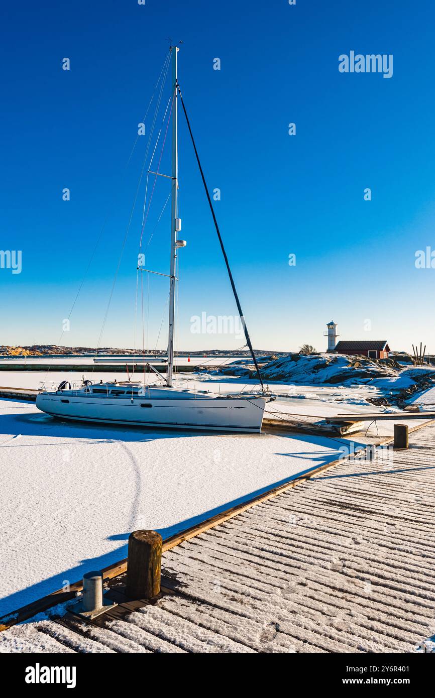 Ein Segelboot ruht in den eisigen Gewässern eines gefrorenen Hafens in Göteborg, Schweden, umgeben von schneebedeckten Docks und klarem blauen Himmel, der die esse einfängt Stockfoto