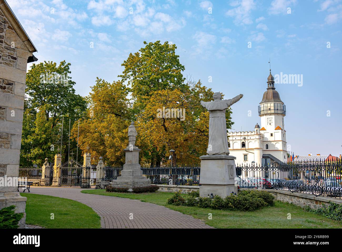 Ein heiteres Bild einer heiligen-Statue, dessen Arme in einer einladenden Geste angehoben wurden, vor dem historischen Szydłowiec-Turm. Herbstlaub und friedlicher Weg Stockfoto