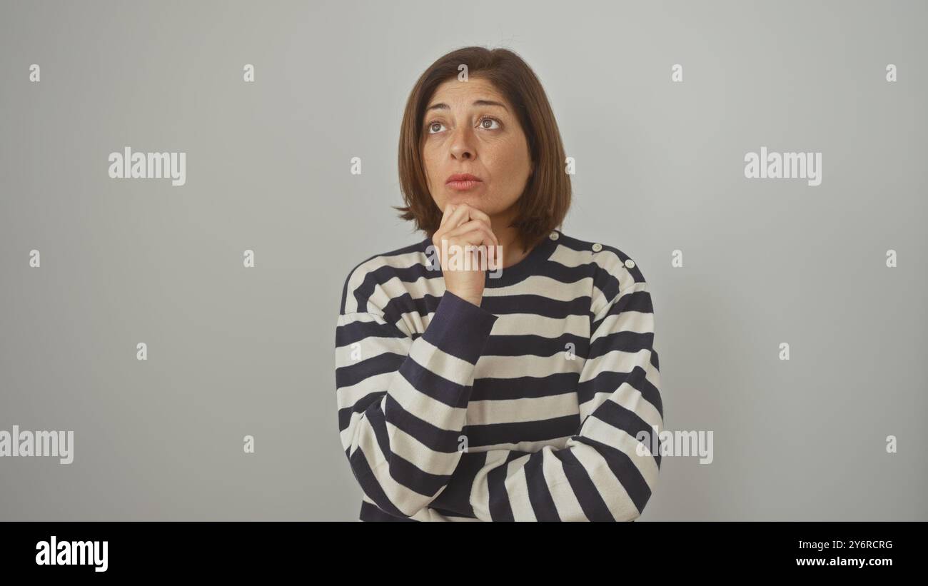 Eine nachdenkliche hispanische Frau mittleren Alters in einem gestreiften Pullover steht vor einem weißen isolierten Hintergrund. Stockfoto