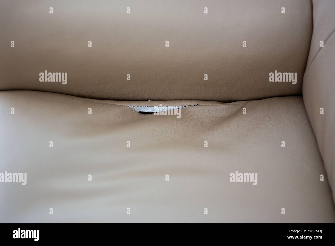 Kunstledersofa mit gerissenen Nähten. Kreativer beigefarbener Hintergrund, Lederstruktur. Stockfoto