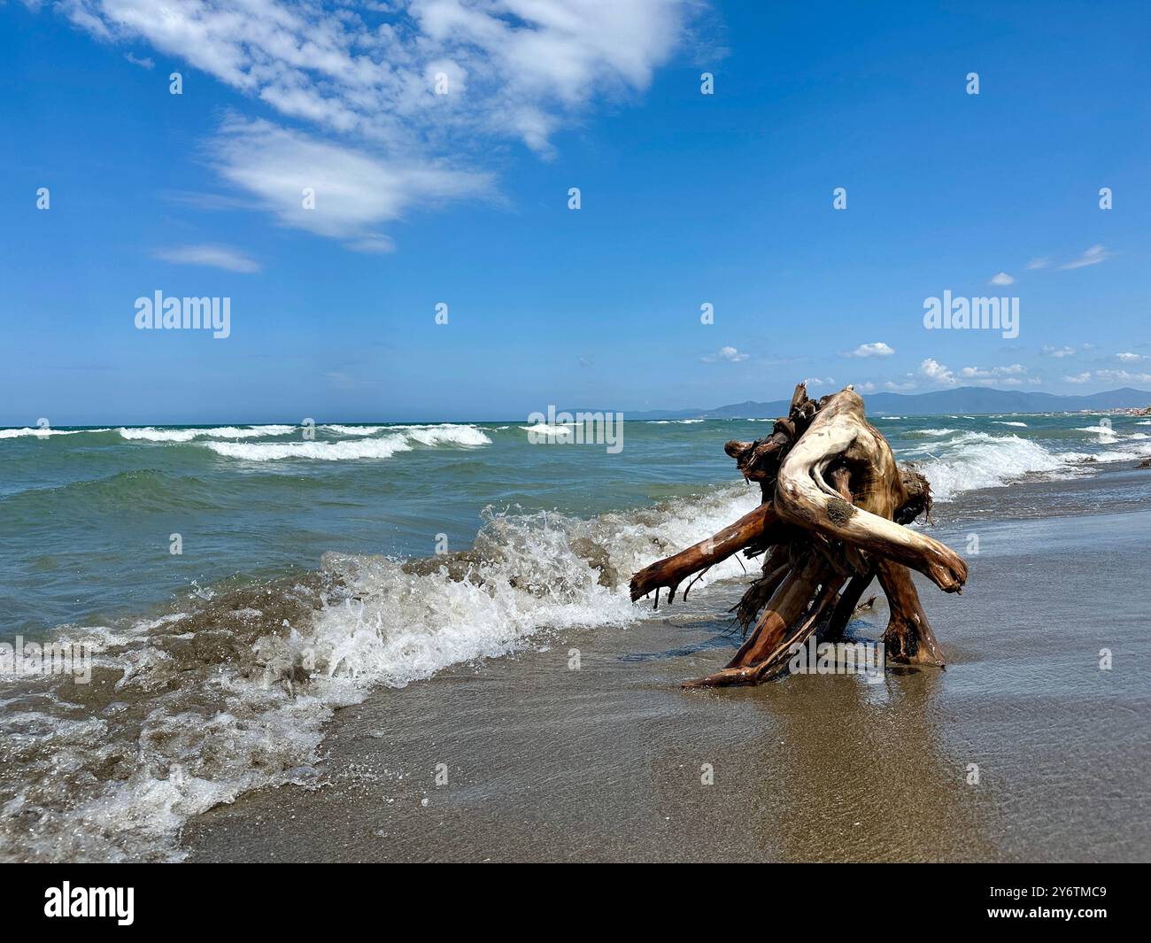 Das Bild zeigt einen italienischen Strand am Meer im Sommer mit einer Nahaufnahme eines Holzelements im Vordergrund. - Smartphone-aufgenommenes Stockfoto
