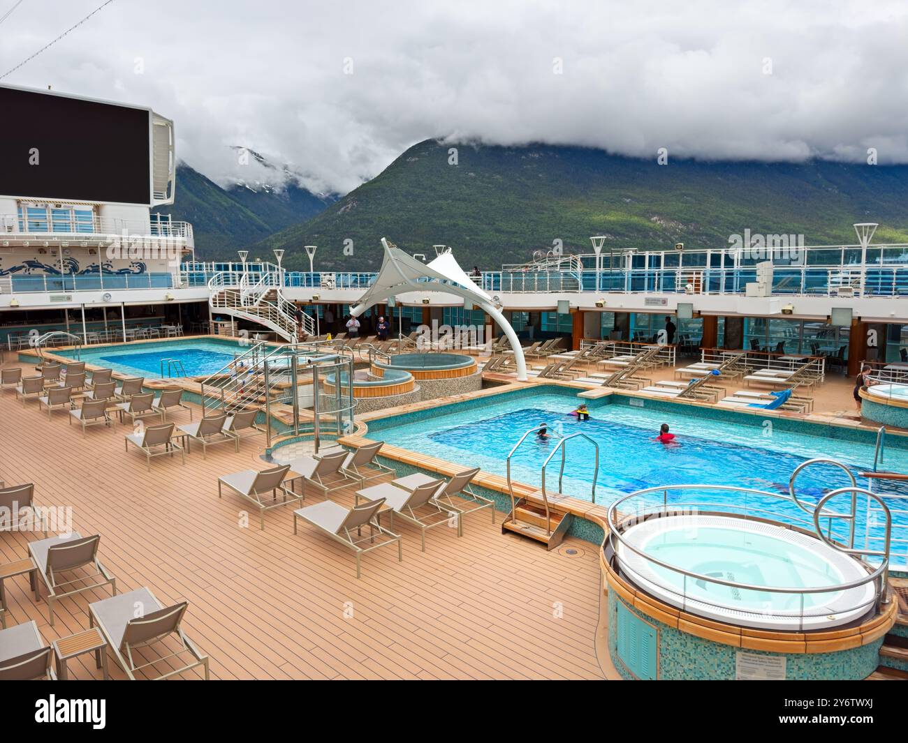 Ein paar Passagiere genießen das Pooldeck auf dem Kreuzfahrtschiff Discovery Princess, während sie an einem wolkenbedeckten Morgen in Skagway anlegen. Stockfoto