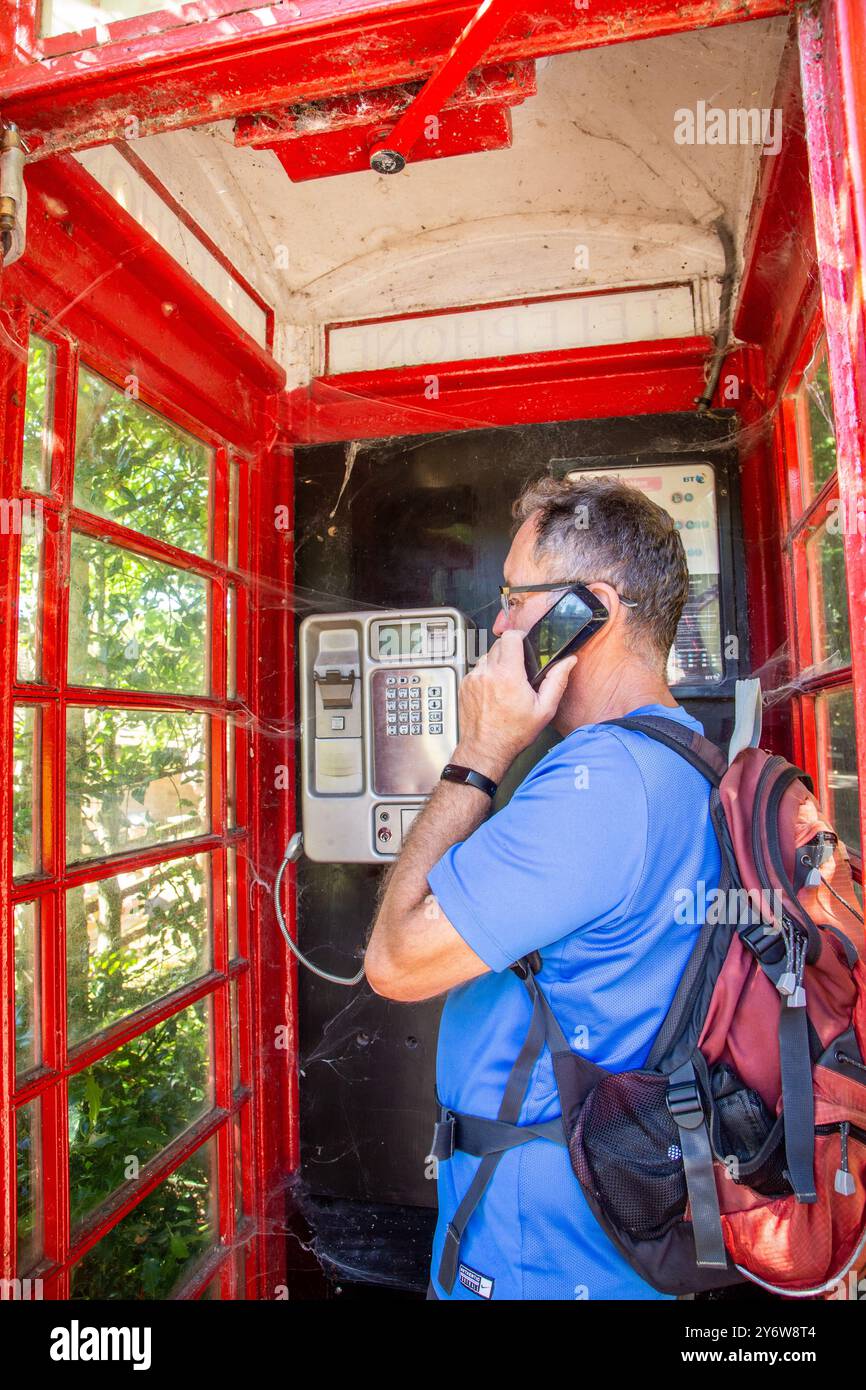 Mann, der mit einem Telefon spricht, in einem traditionellen roten englischen Telefonkastendesign Nr. 6 / K6, entworfen 1935 von Sir Gilbert Scott Stockfoto
