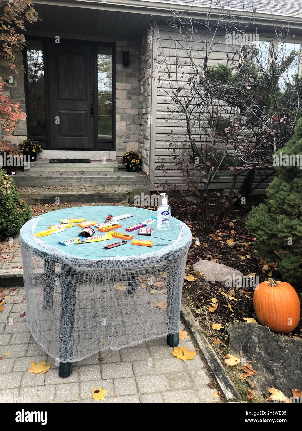 Halloween-Leckereien und Handdesinfektionsmittel stehen auf einem Tisch vor dem Haus, sodass Kinder unter Wahrung sozialer Distanz „Trick-or-Treat“-Effekte genießen können. Stockfoto