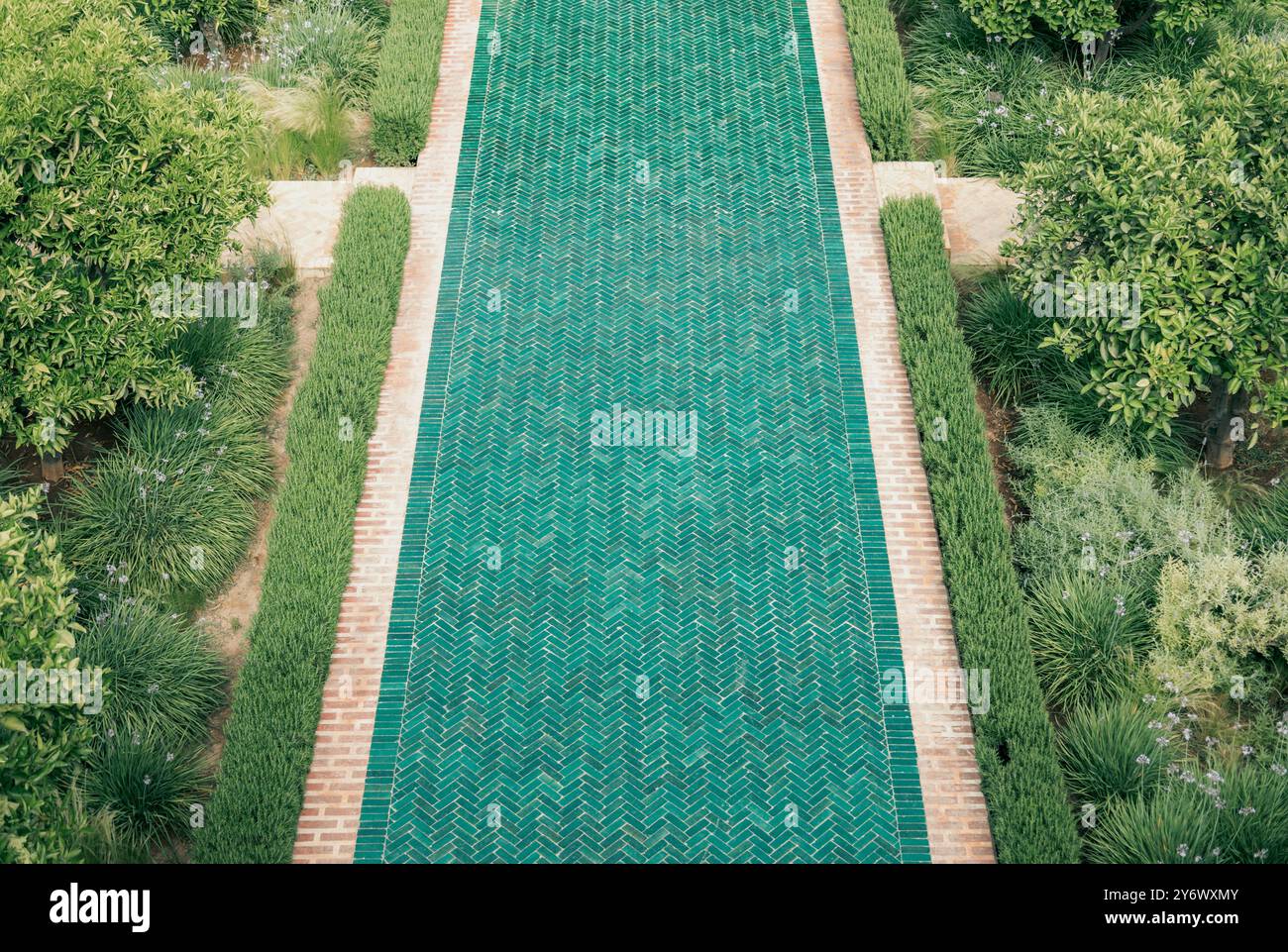 Blick aus der vogelperspektive auf den zentralen grünen marokkanischen Fliesenweg durch Le Jardin Secret, botanischer Garten Marrakesch, mit üppigen Pflanzen und Bäumen an der Seite, Marokko Stockfoto