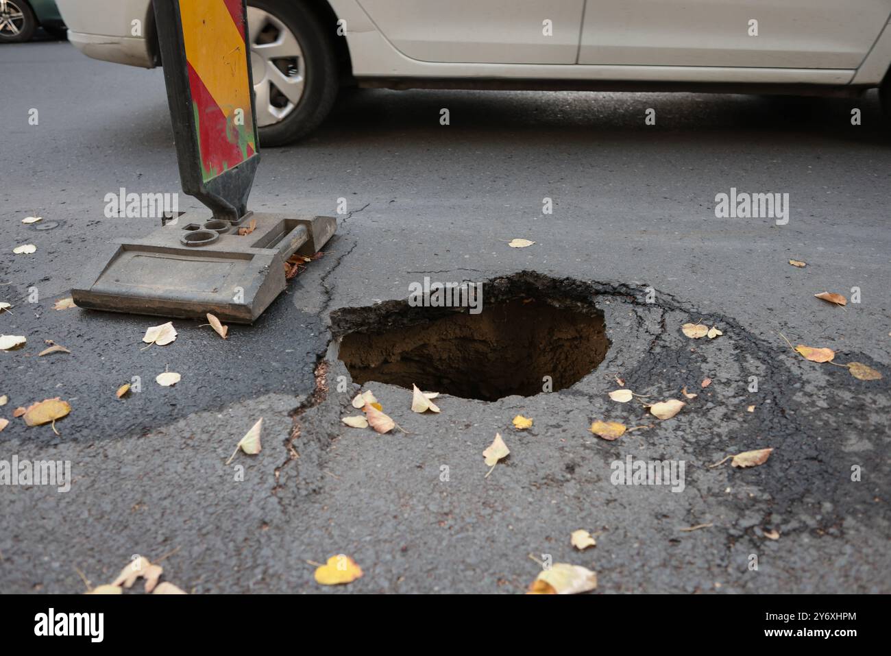 Details mit einem großen Schlagloch mitten auf einer asphaltierten Straße mit vorbeifahrenden Autos Stockfoto