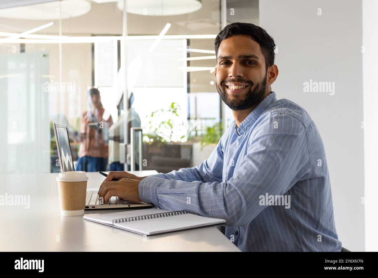 Arbeiten am Laptop, Mann lächelt mit Kaffeetasse und Notebook im Büro Stockfoto