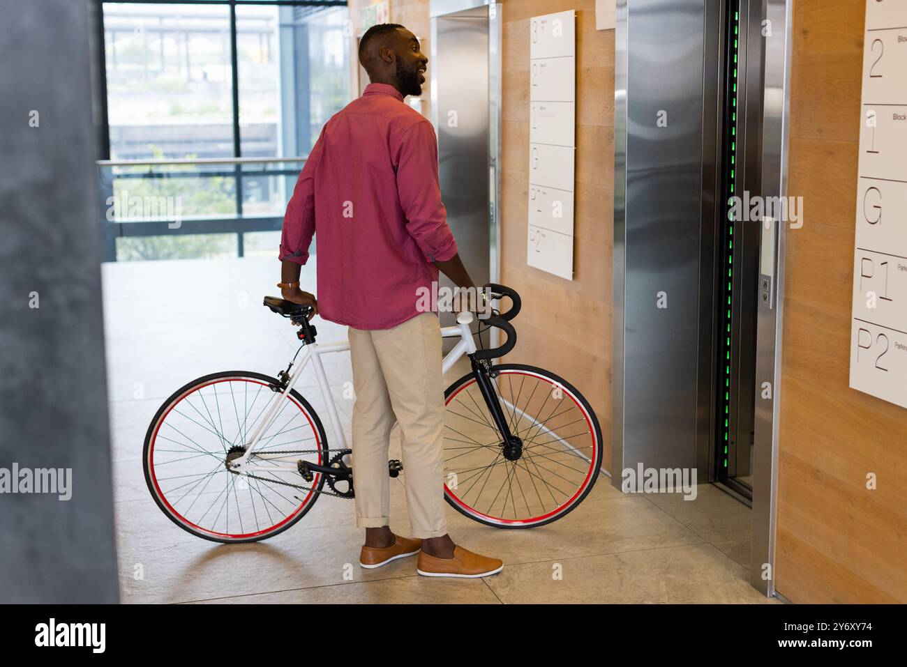 Mann mit Fahrrad, der in der Lobby des modernen Bürogebäudes auf den Aufzug wartet Stockfoto