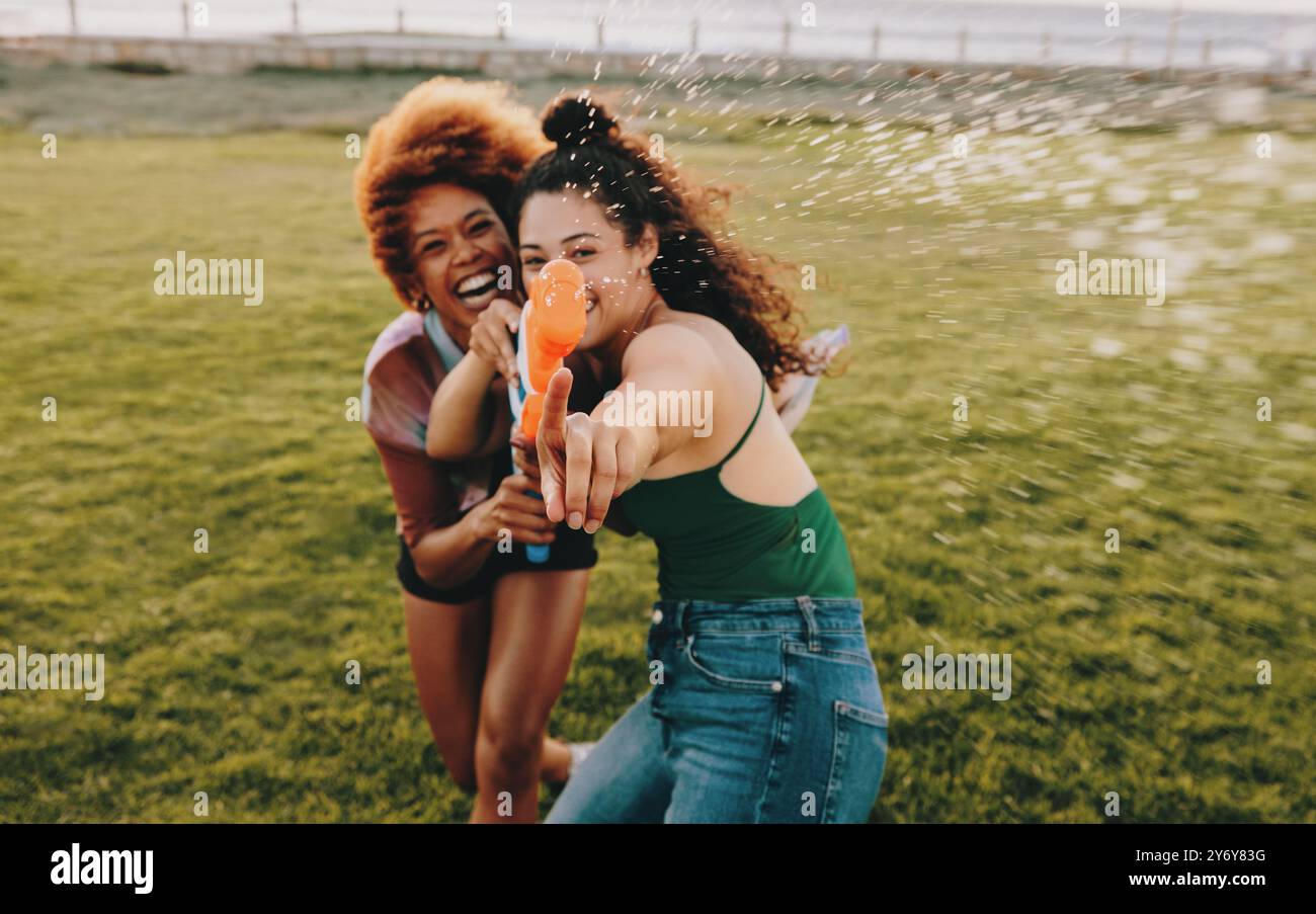 Zwei Mädchen feiern ihre Freundschaft an einem Sommertag, bei einem verspielten Wasserkampf im Freien, der Freude und Lachen ausstrahlt. Stockfoto