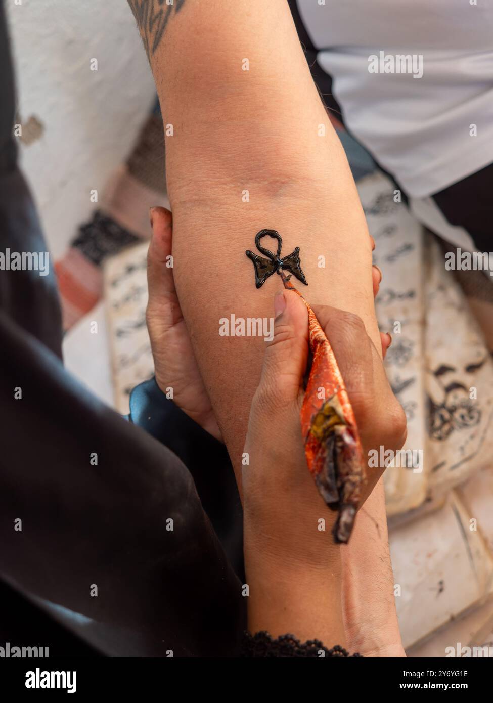 Eine Frau zeichnet ein Tattoo mit Henna auf dem Arm einer Frau. Das Tattoo ist ein ägyptisches Symbol, und die Frau benutzt einen Henna-Pinsel, um es zu kreieren. Szene Stockfoto