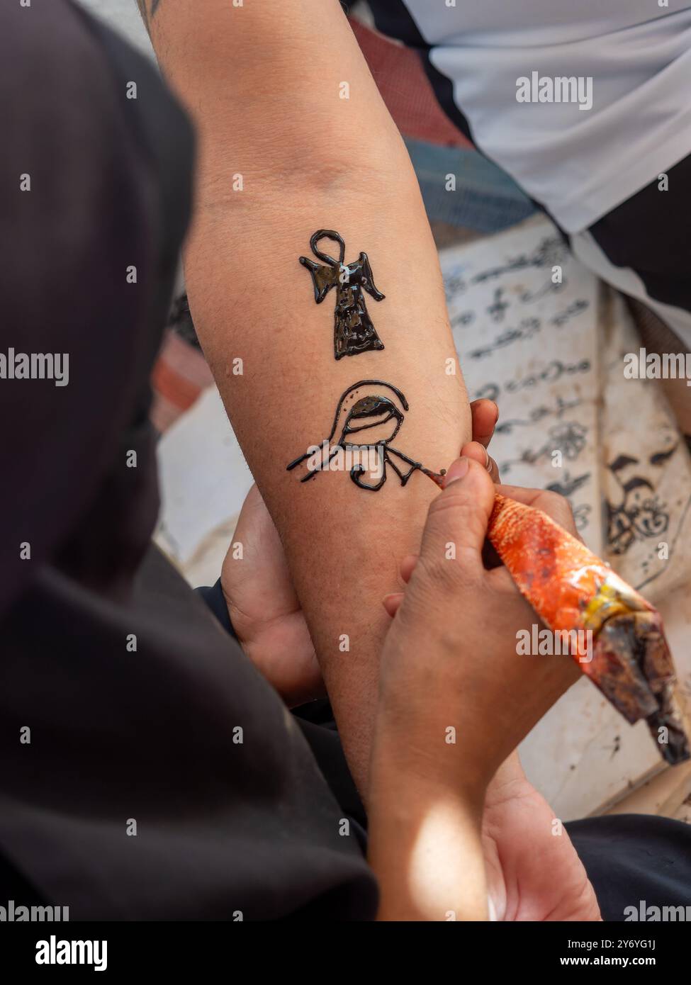 Eine Nubierin zeichnet ein Tattoo mit Henna auf den Arm einer Frau. Das Tattoo ist ein ägyptisches Symbol, und die Frau benutzt einen Henna-Pinsel, um es zu kreieren Stockfoto