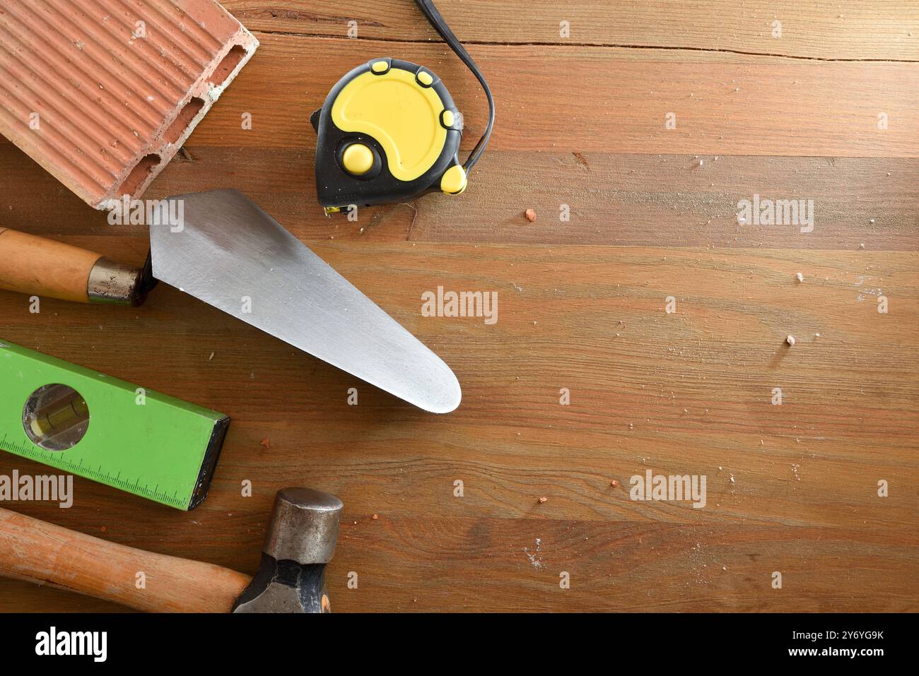 Bauwerkzeuge wie Kelle, Waage, Bandmaß, Hammer und Ziegel auf Holzdiele. Draufsicht. Stockfoto