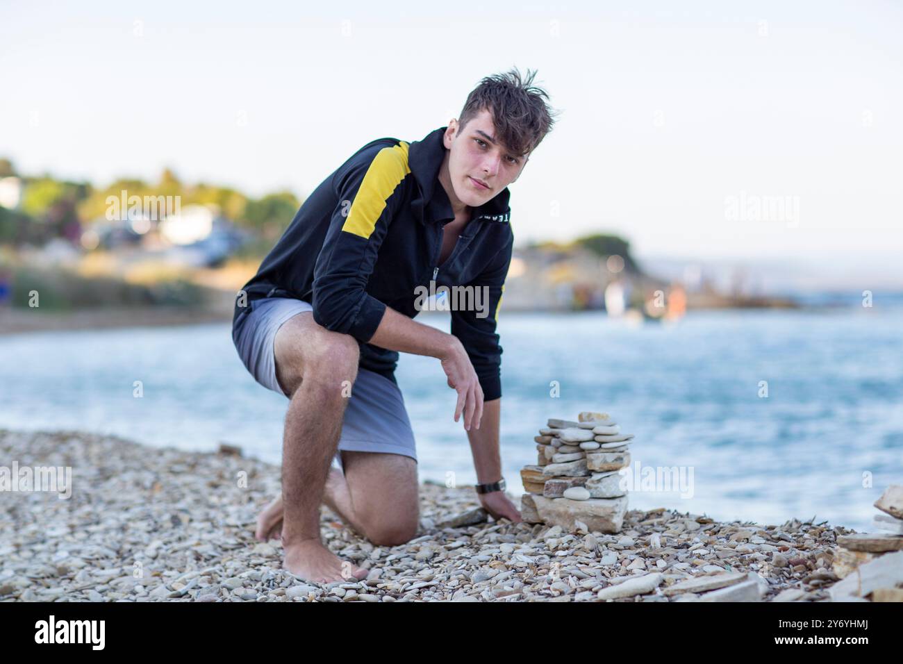 Hübscher junger Mann, der eine Pyramide aus Steinen am Meer baut Stockfoto
