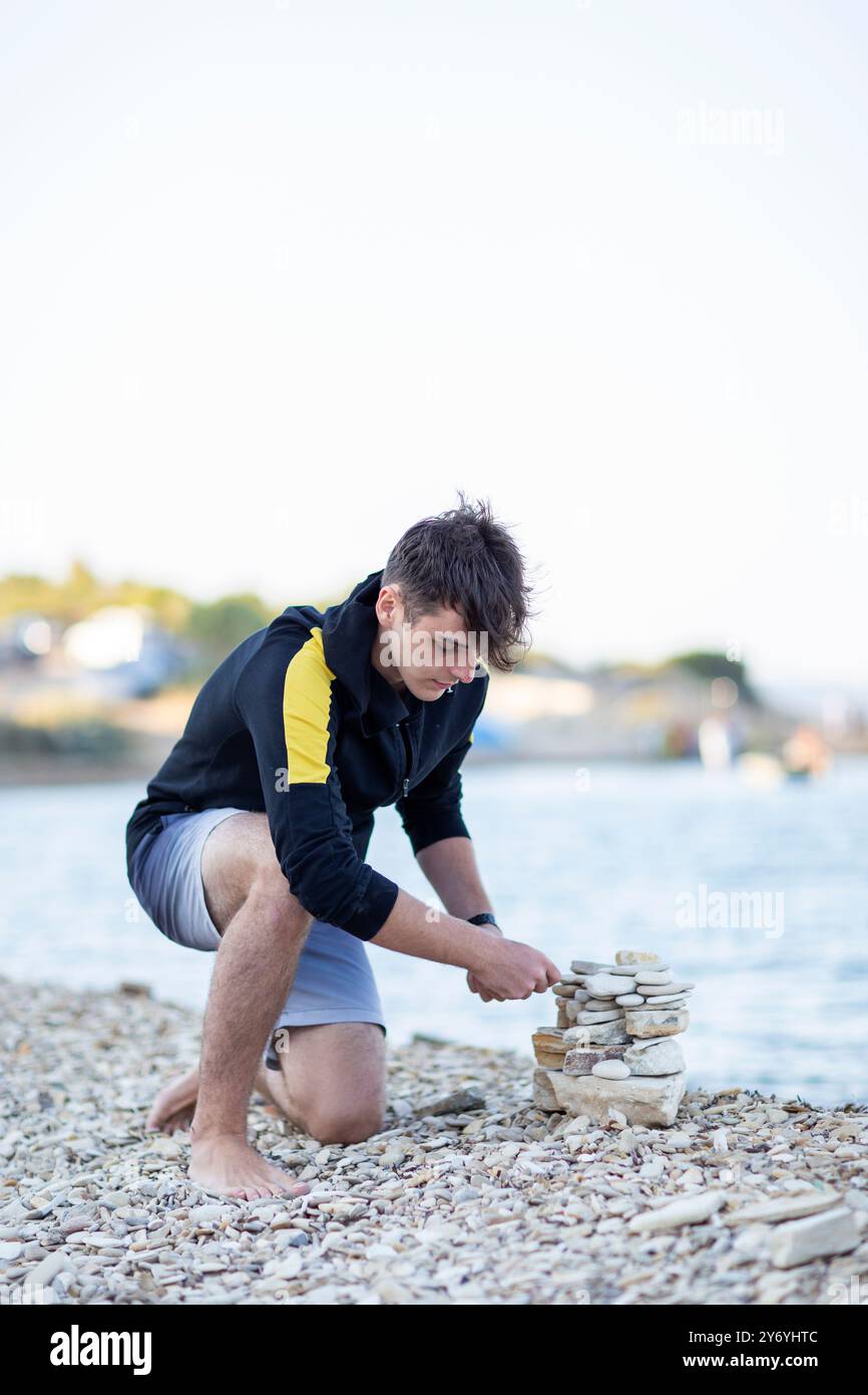 Hübscher junger Mann, der eine Pyramide aus Steinen am Meer baut Stockfoto