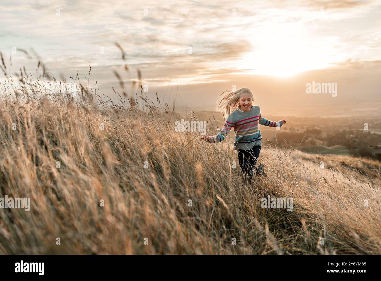 Glückliche Frau, die in schönem Licht durch das goldene Feld läuft Stockfoto