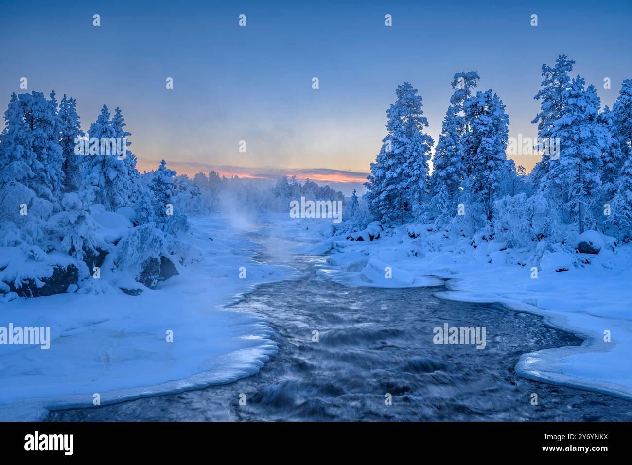 Dampfender Juutuanjoki-Fluss mit Wald und schneebedeckter Umgebung bei Sonnenuntergang und winterlicher blauer Stunde in Inari (Lappland, Finnland) Stockfoto