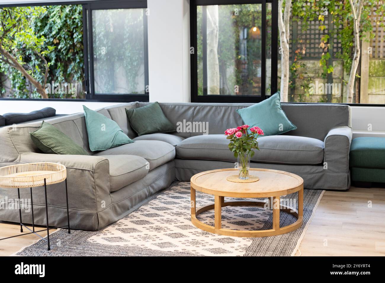 Graues Schlafsofa, hölzerner Kaffeetisch und Herzstück mit Blumenmuster im modernen Wohnzimmer, zu Hause Stockfoto