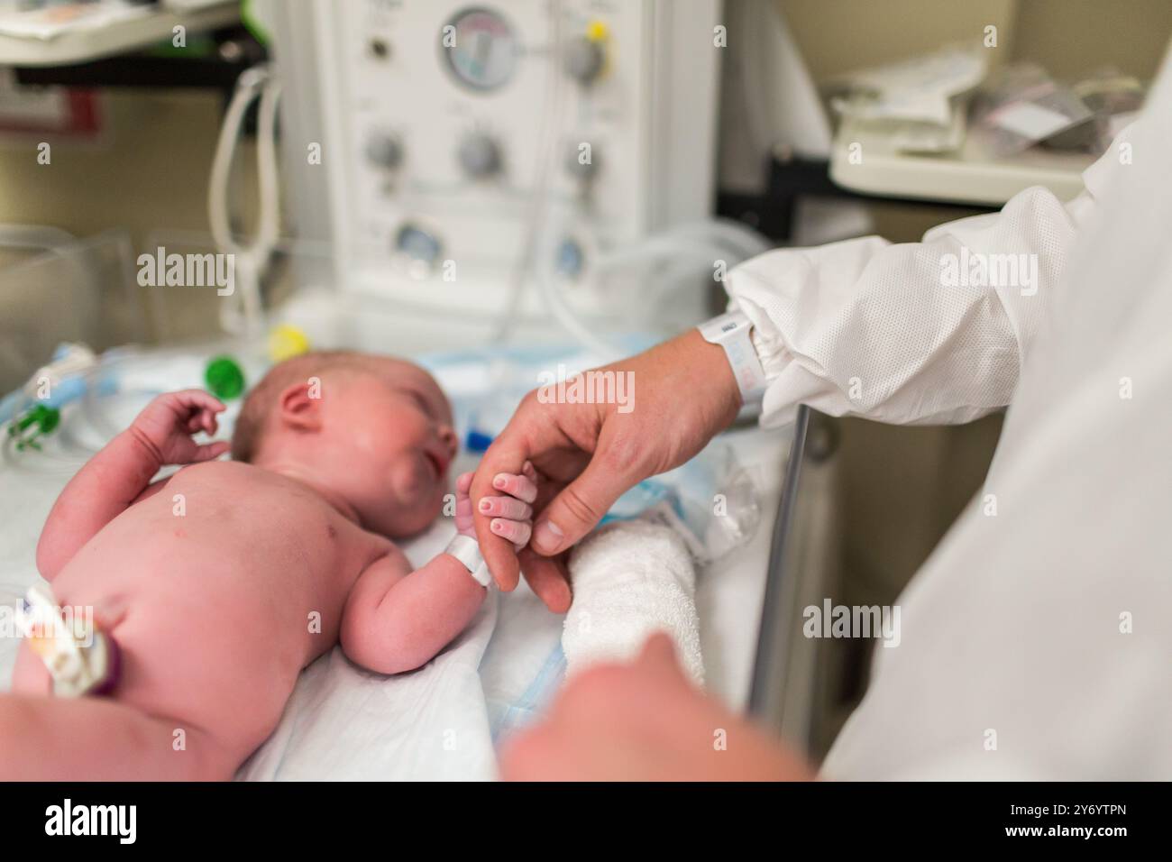 Das Neugeborene hält Dads Finger auf dem Wärmebett Stockfoto