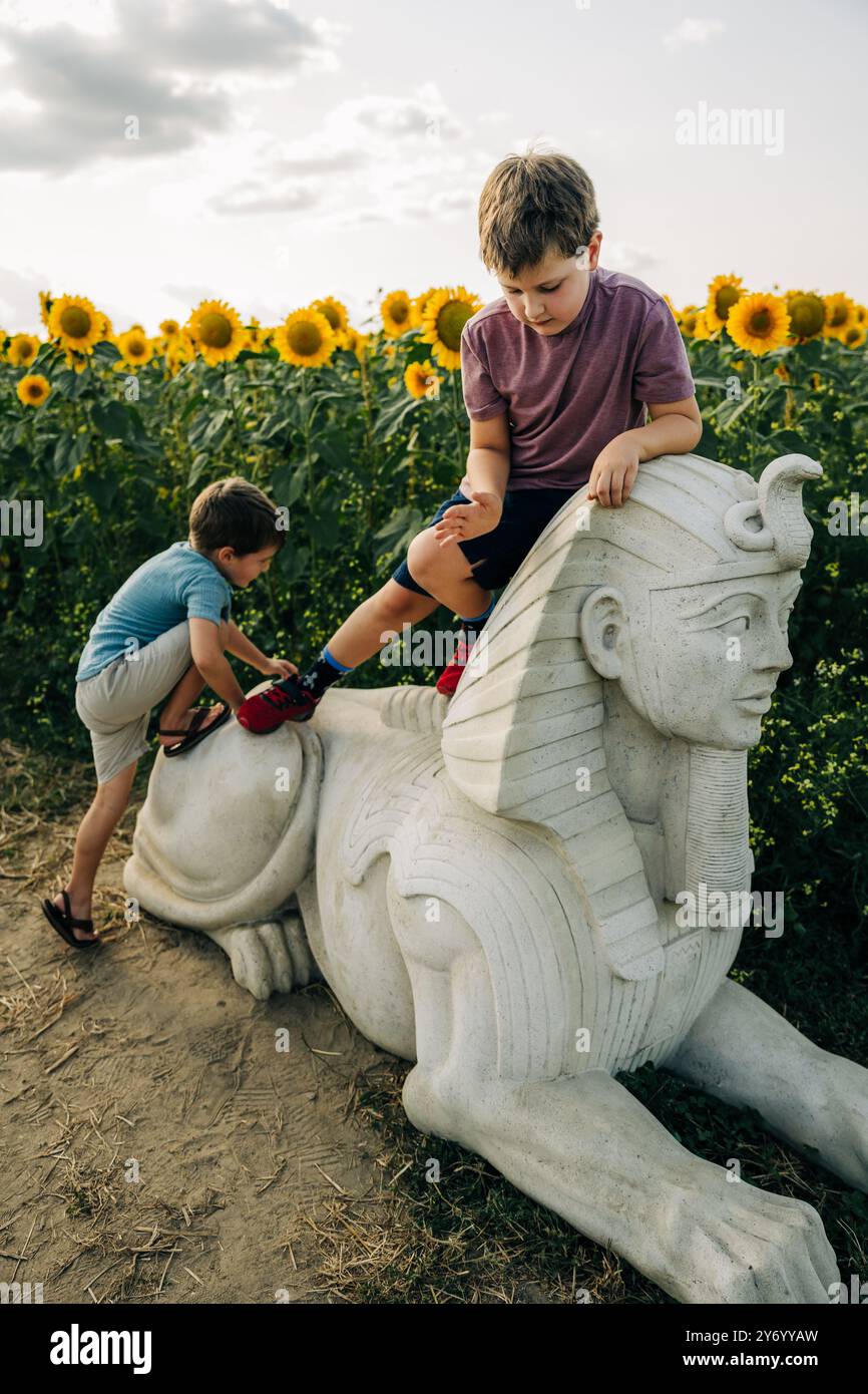 Kinder spielen auf einer Sphinx-Statue auf einem Sonnenblumenfeld Stockfoto