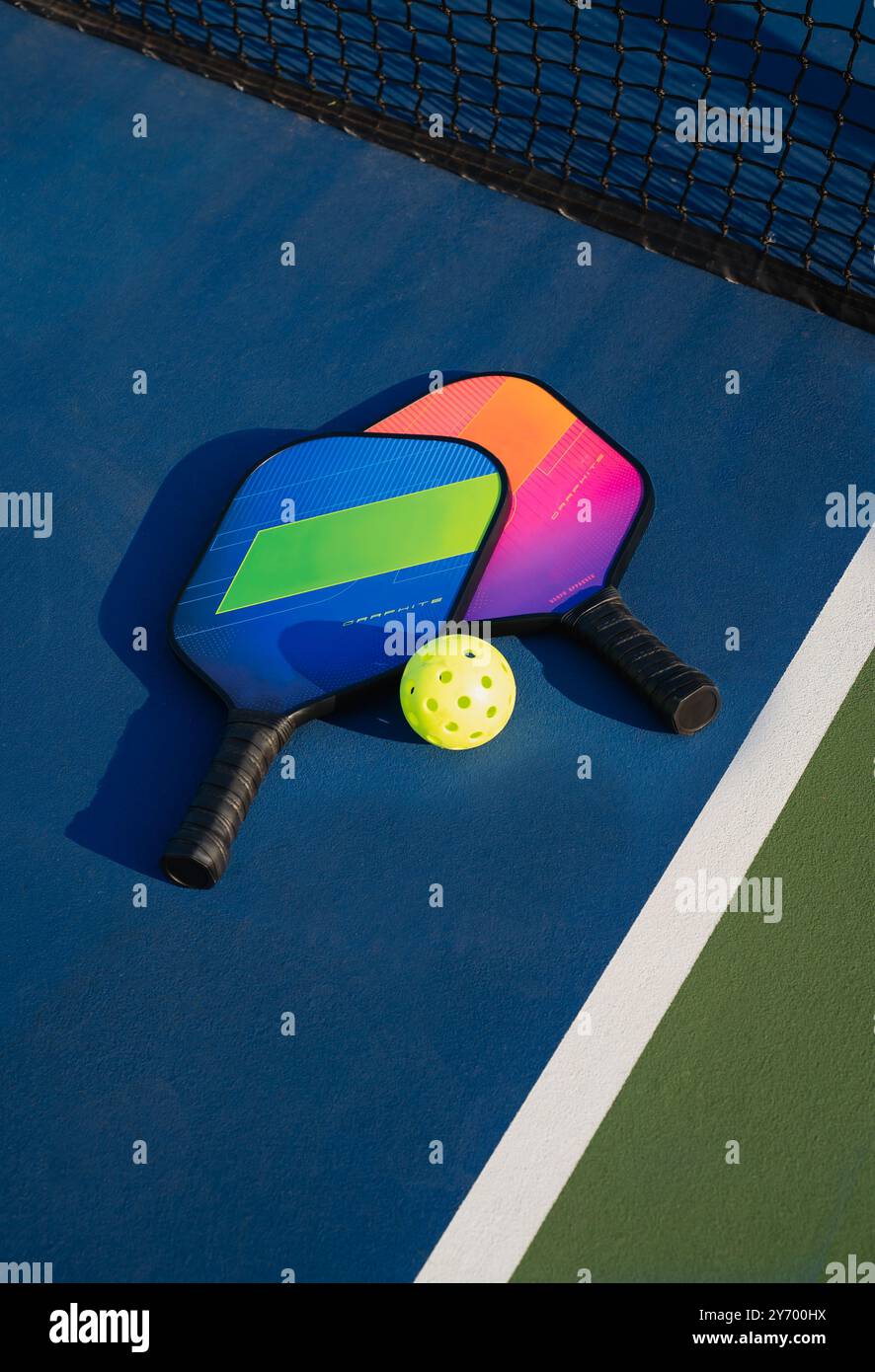 Nahaufnahme von Pickleball-Paddeln und Ball neben dem Netz auf dem blauen Platz. Stockfoto