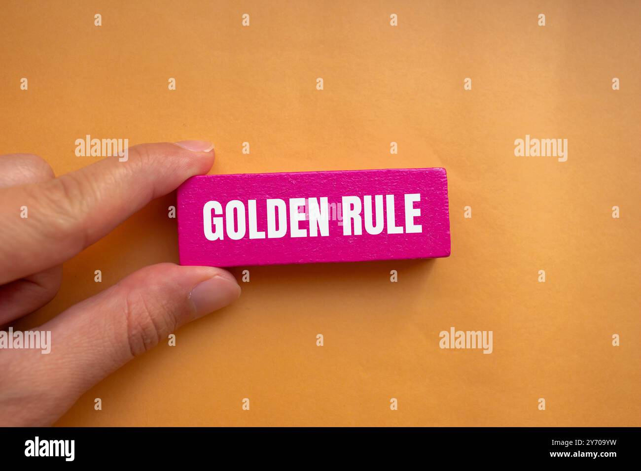 Goldene Regelnachricht auf rosa Holzblock mit orangem Hintergrund. Konzeptionelles goldenes Regelsymbol. Kopierbereich. Stockfoto