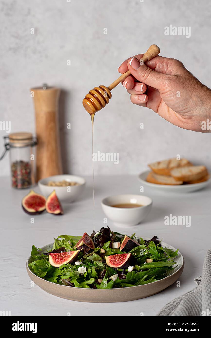 Lebensmittelfotografie von Salat mit Feigen und Fetakäse, Spinat, Salat, Honig, Pinienkernen, geröstetes Brot, gedeckter Tisch, Honig von Hand auf einen Salat gießen Stockfoto