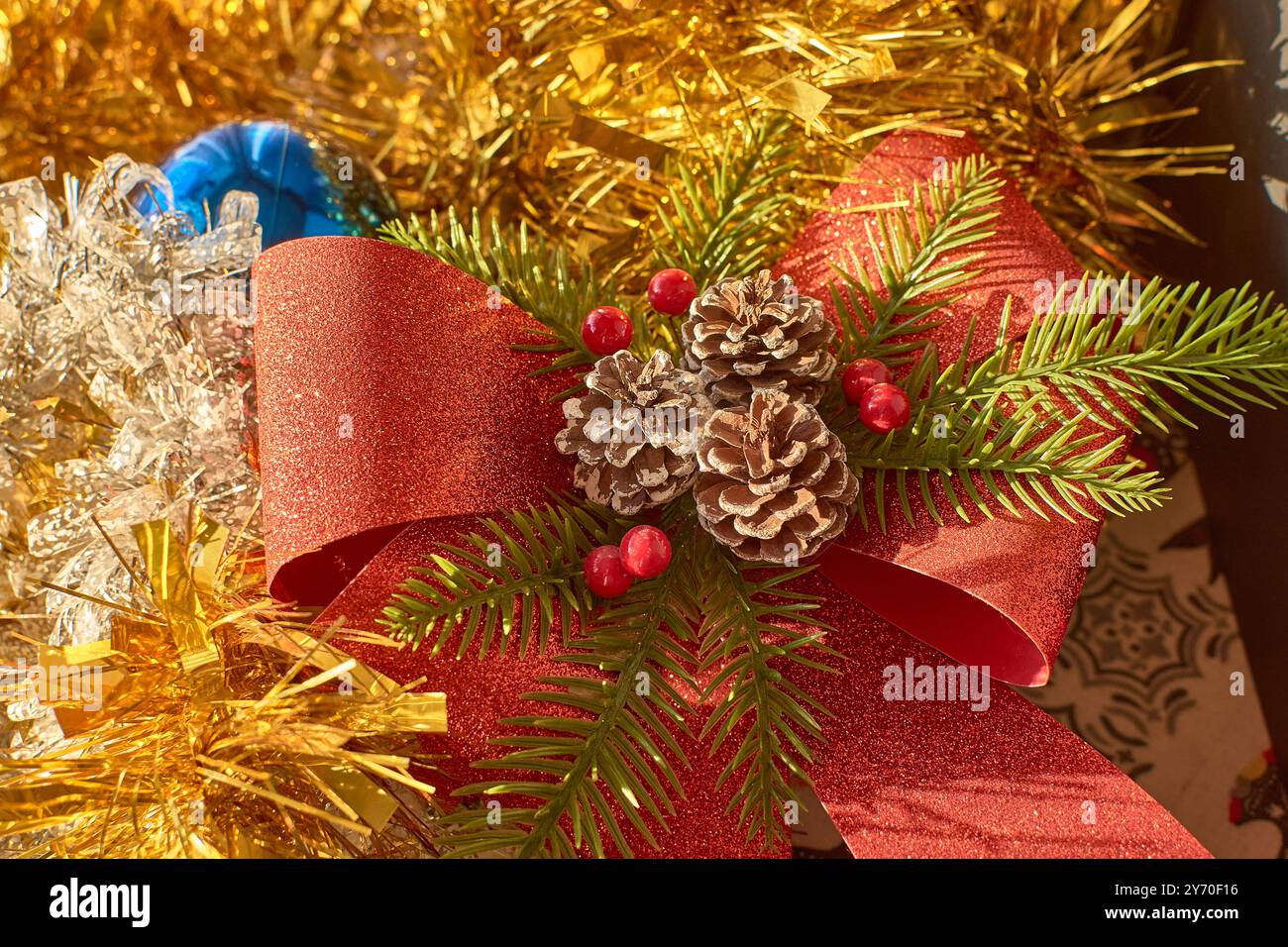 Eine farbenfrohe und festliche Weihnachtsdekoration mit einer hellblauen Kugel, umgeben von einer funkelnden roten Schleife, Tannenzapfen und immergrünen Zweigen mit Stockfoto