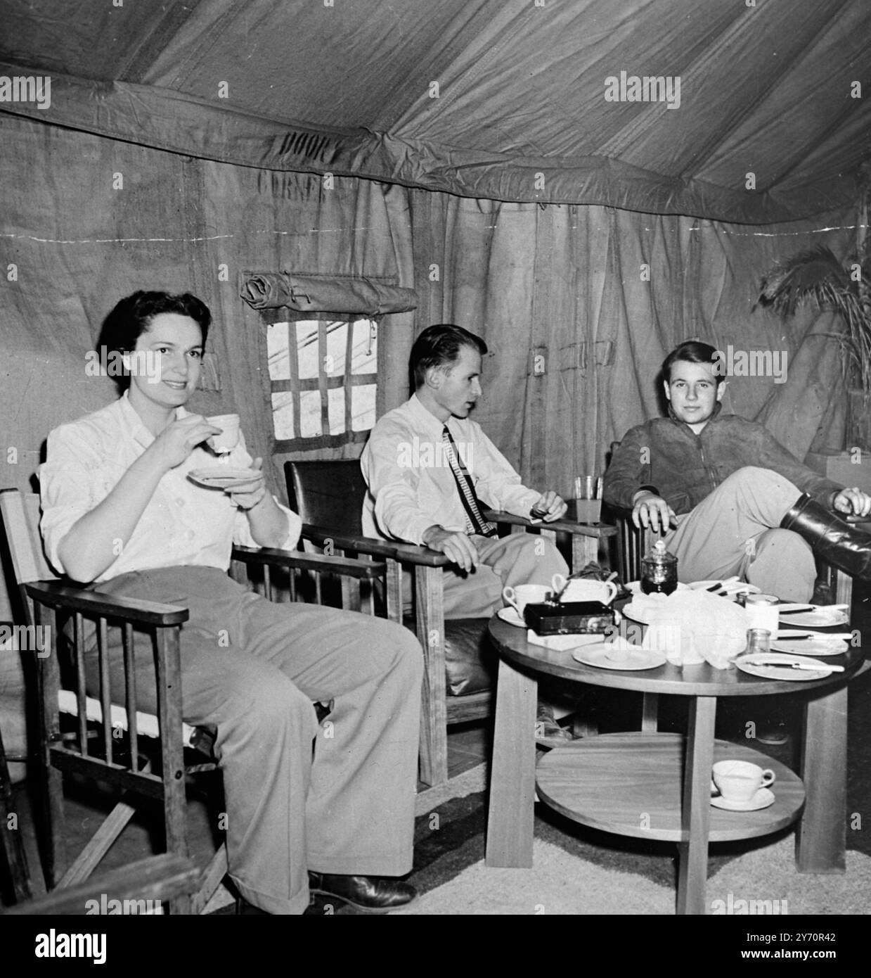 73 Jahre alter Aga Khan 'Croesus' auf Safari. In der Lounge des Hauptspeisesaals im Herzen des Dschungels. Der Begum Aga Khan trinkt Tee mit Wendell Phillips, Leiter der Afrika-Expedition der Universität von Kalifornien, Zentrum und rechts, Prinz Sadrudin - dem jüngsten Sohn des Aga Khans. Sie waren auf Safari, um wilde Tiere im ostafrikanischen Dschungel zu fotografieren. Die Expedition kostete USD4000 pro Tag und das Lager war mit herrlichen und komfortablen Wohnungen ausgestattet. 1950 Stockfoto